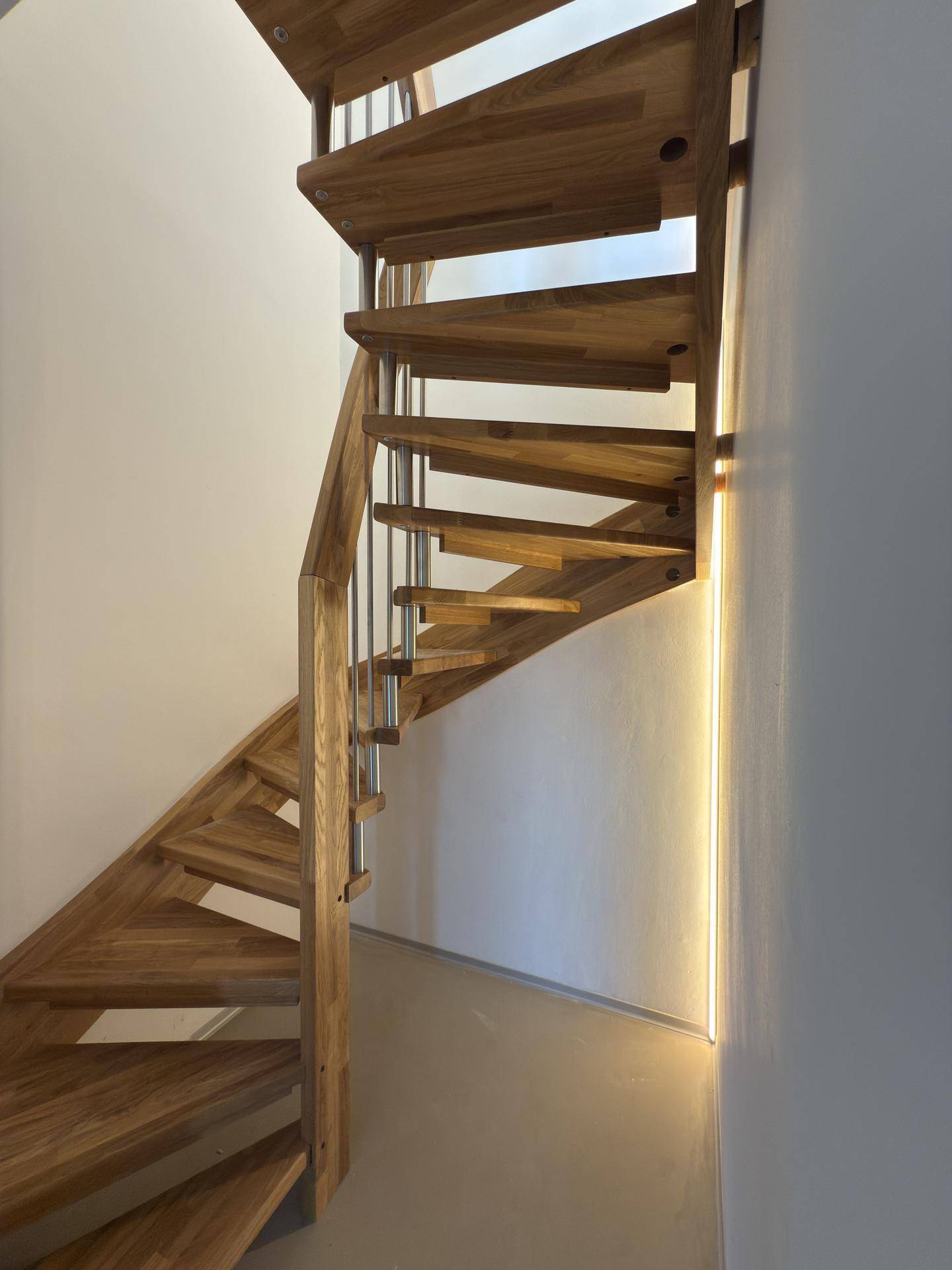 Elegante Holztreppe mit Metallgeländer und indirekter Beleuchtung im Flurbereich.