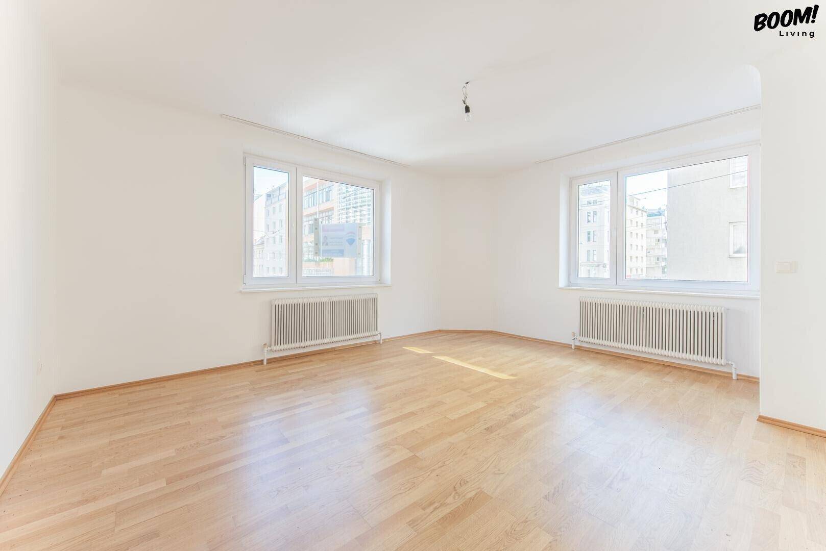 Geräumiges, helles Wohnzimmer mit zwei großen Fenstern und schönem Parkettboden.