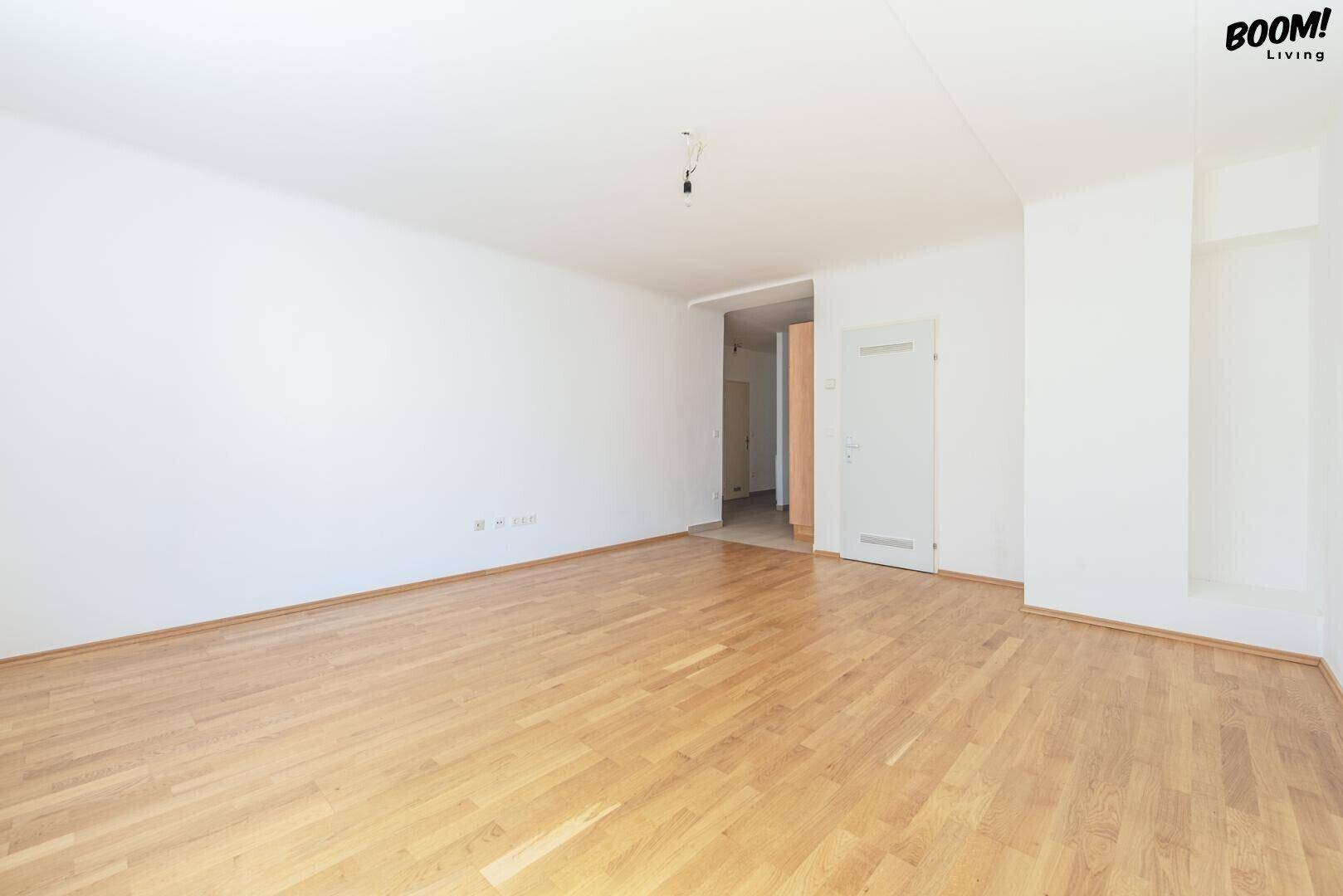 Großes, leeres Zimmer mit Parkettboden und offenem Zugang zu einem weiteren Bereich.