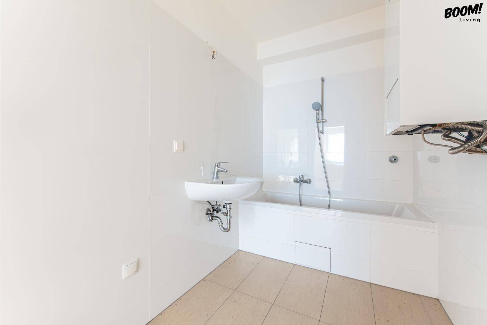 Helles Badezimmer mit weißen Fliesen, Waschbecken und Badewanne mit Duschfunktion.