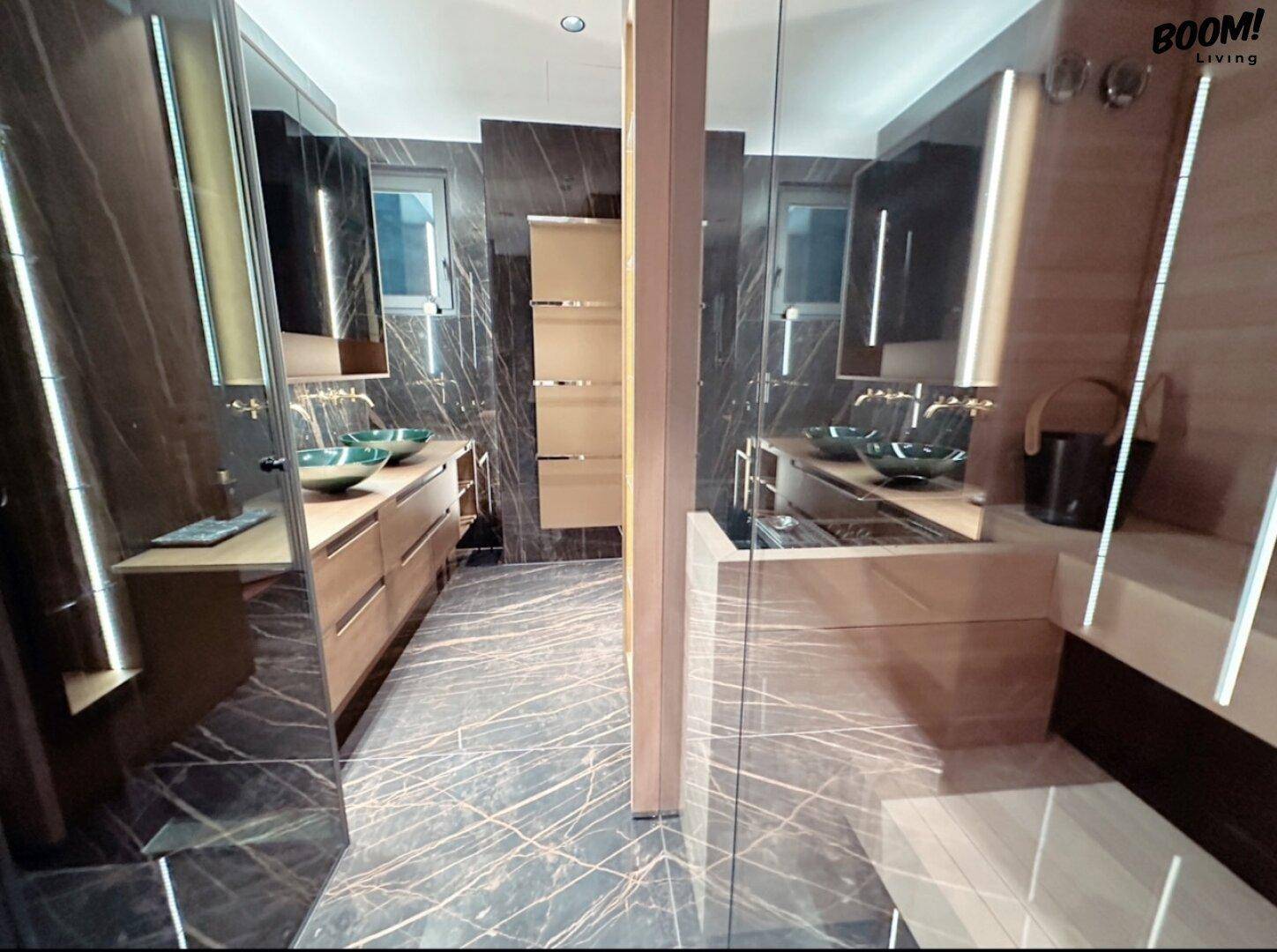 Elegantes Badezimmer mit dunklen Marmoroberflächen, zwei Waschbecken und integrierter Beleuchtung.