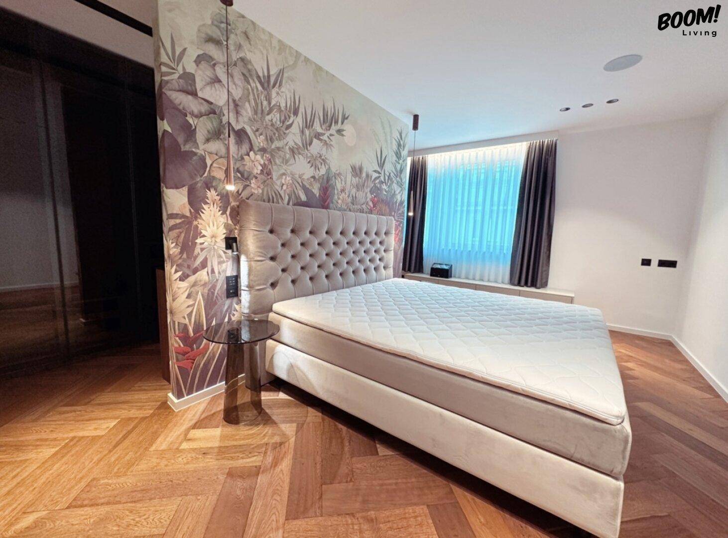 Helles Schlafzimmer mit Fischgrätparkett, gepolstertem Bett und dekorativer Wandgestaltung.