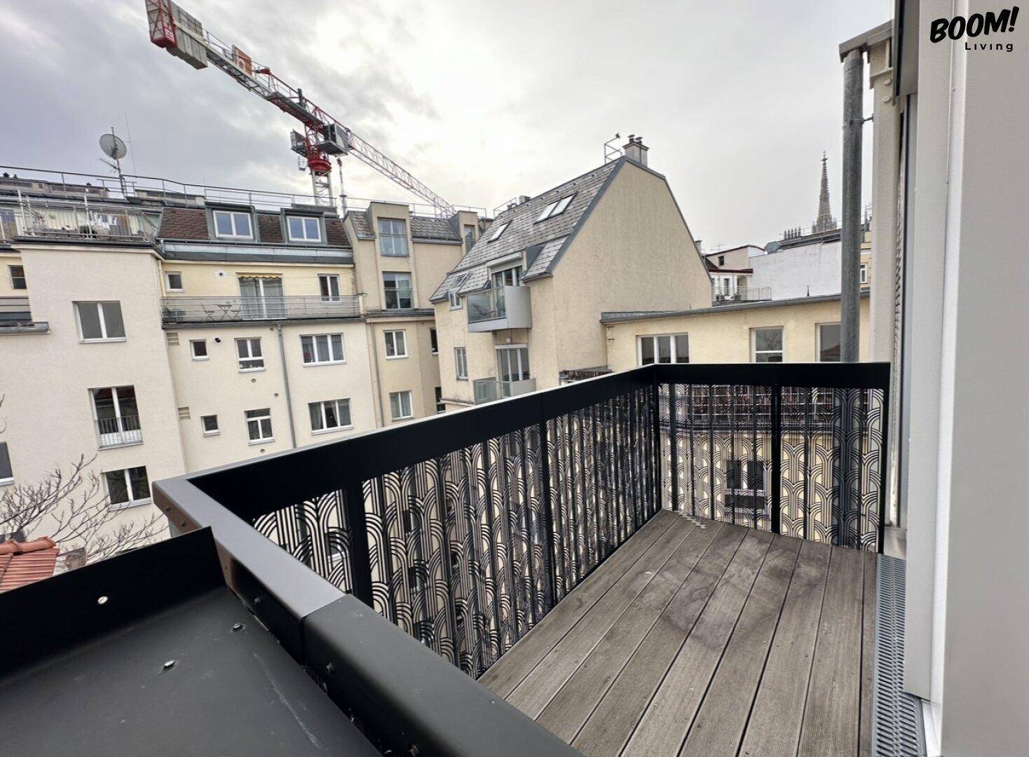 Kleiner Balkon mit Holzboden und Blick auf die umliegenden Gebäude und einen Baukran.