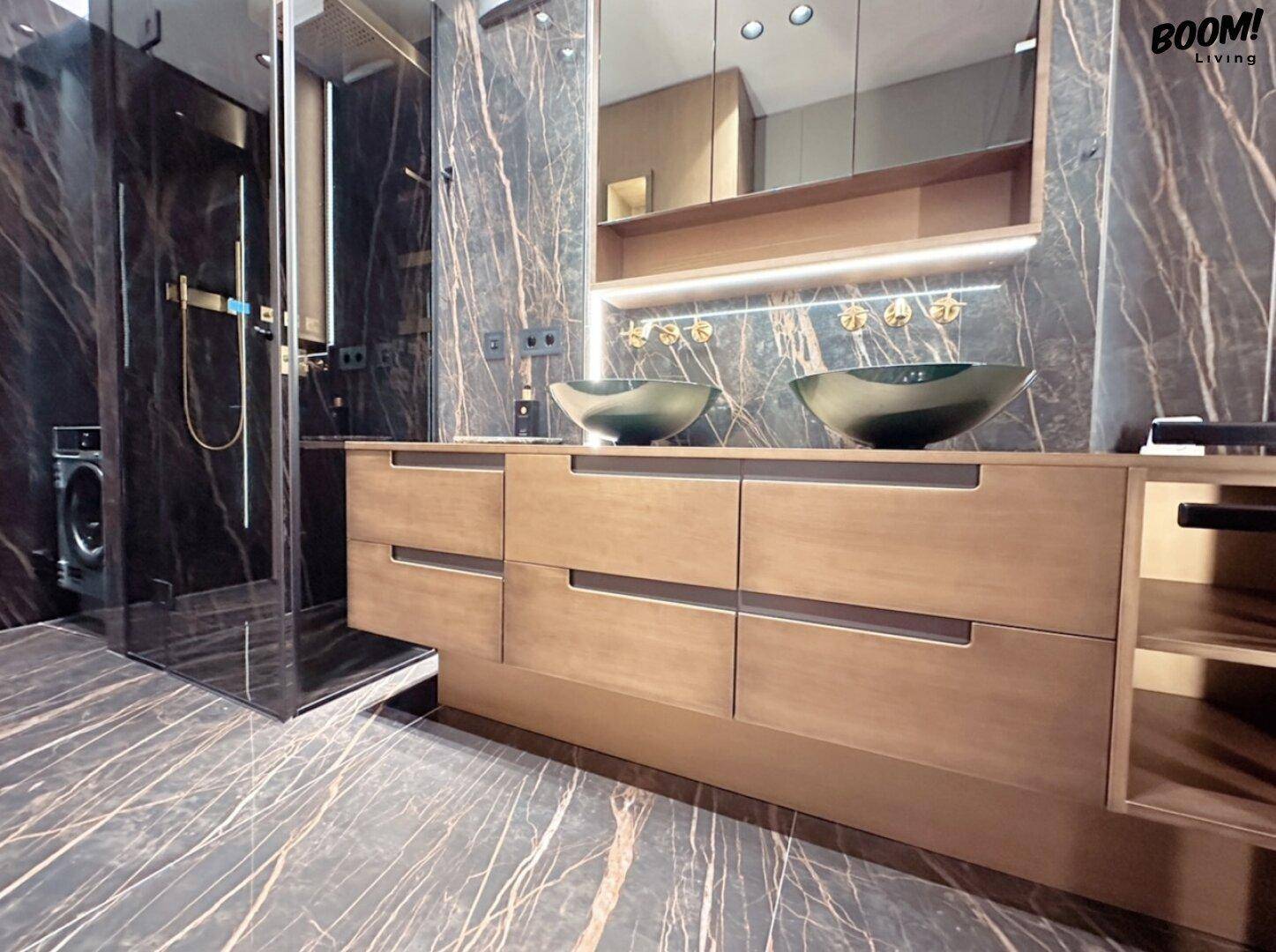Modernes Badezimmer mit dunklen Marmorfliesen, Holzwaschtisch und zwei Aufsatzwaschbecken.