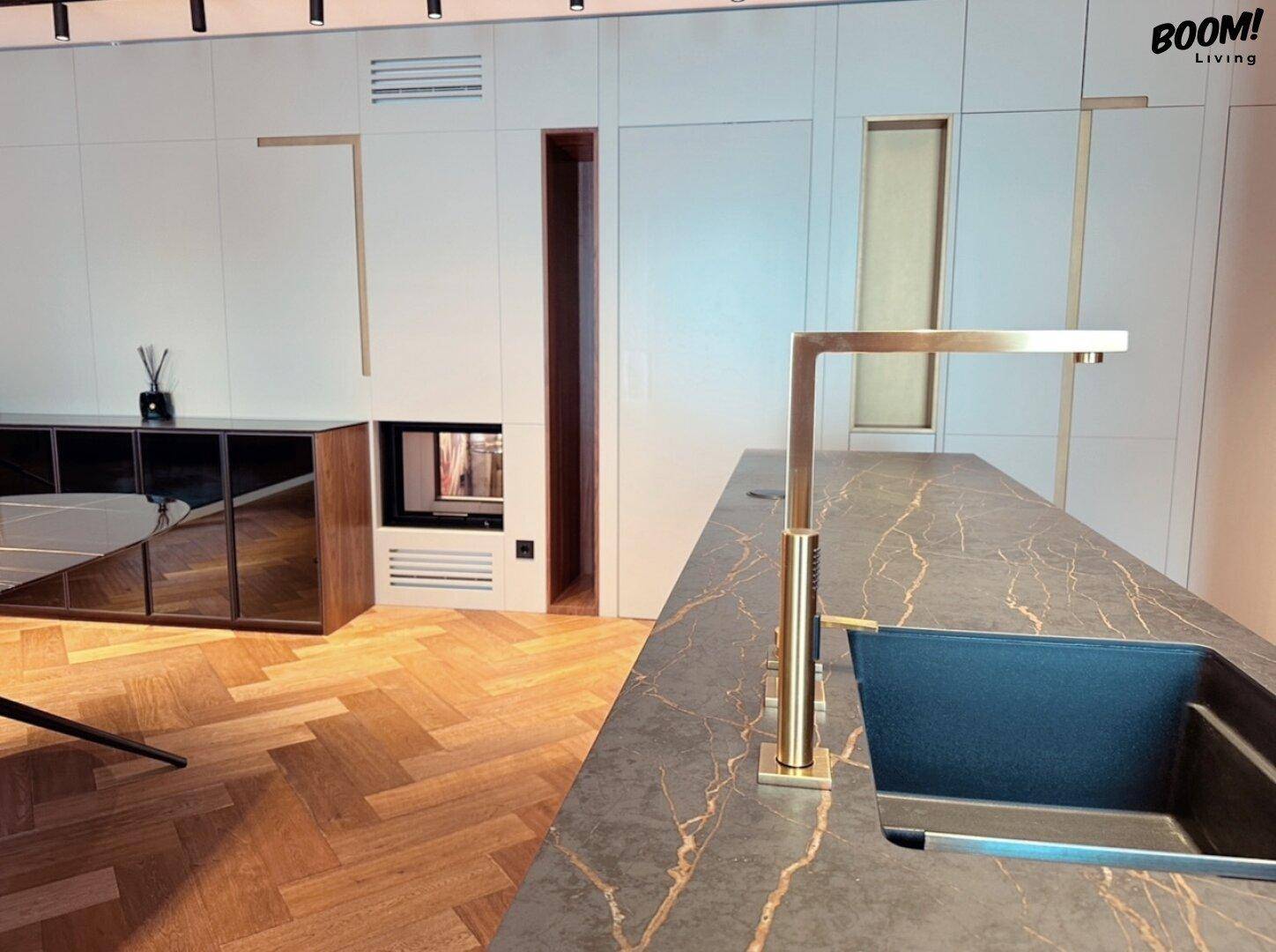 Elegante Küche mit dunkler Arbeitsplatte, goldenen Armaturen und integriertem Kamin im Wohnbereich.