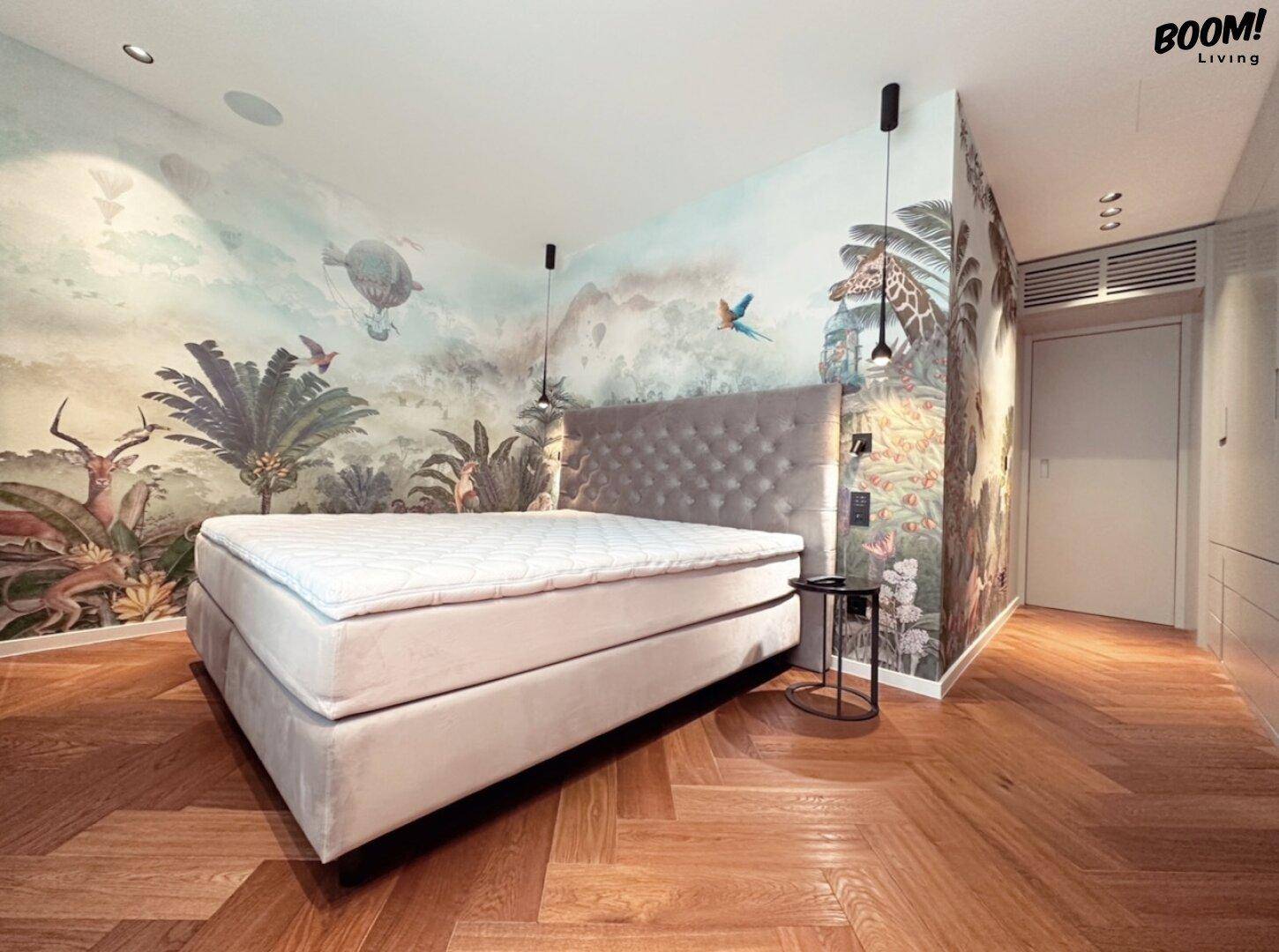 Schlafzimmer mit auffälliger Dschungel-Tapete, gepolstertem Bett und Fischgrätparkettboden.