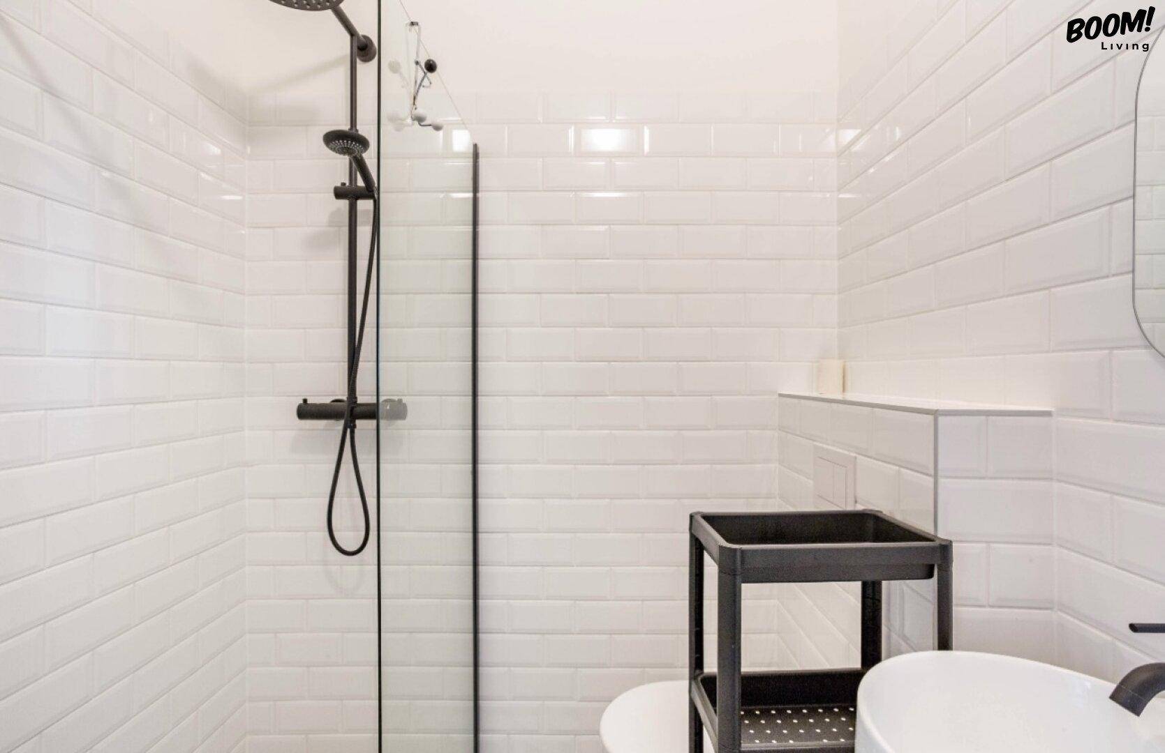 Modernes Badezimmer mit weißen Fliesen, ebenerdiger Dusche und schwarzer Armatur.
