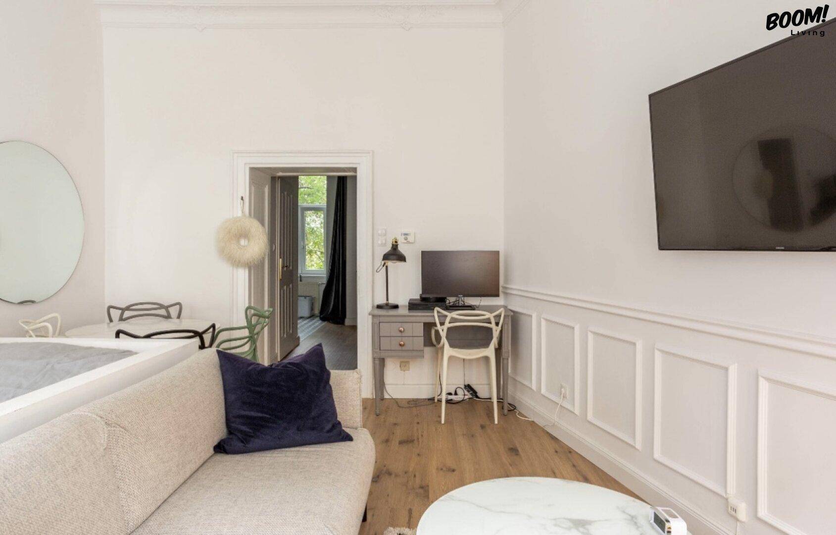 Heller Wohnbereich mit Schreibtisch, Sofa und Wandfernseher, ideal für Home-Office.