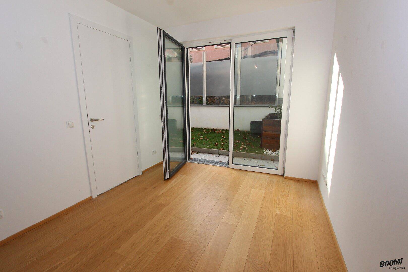 Helles Zimmer mit Holzboden und Zugang zu einem kleinen Außenbereich.
