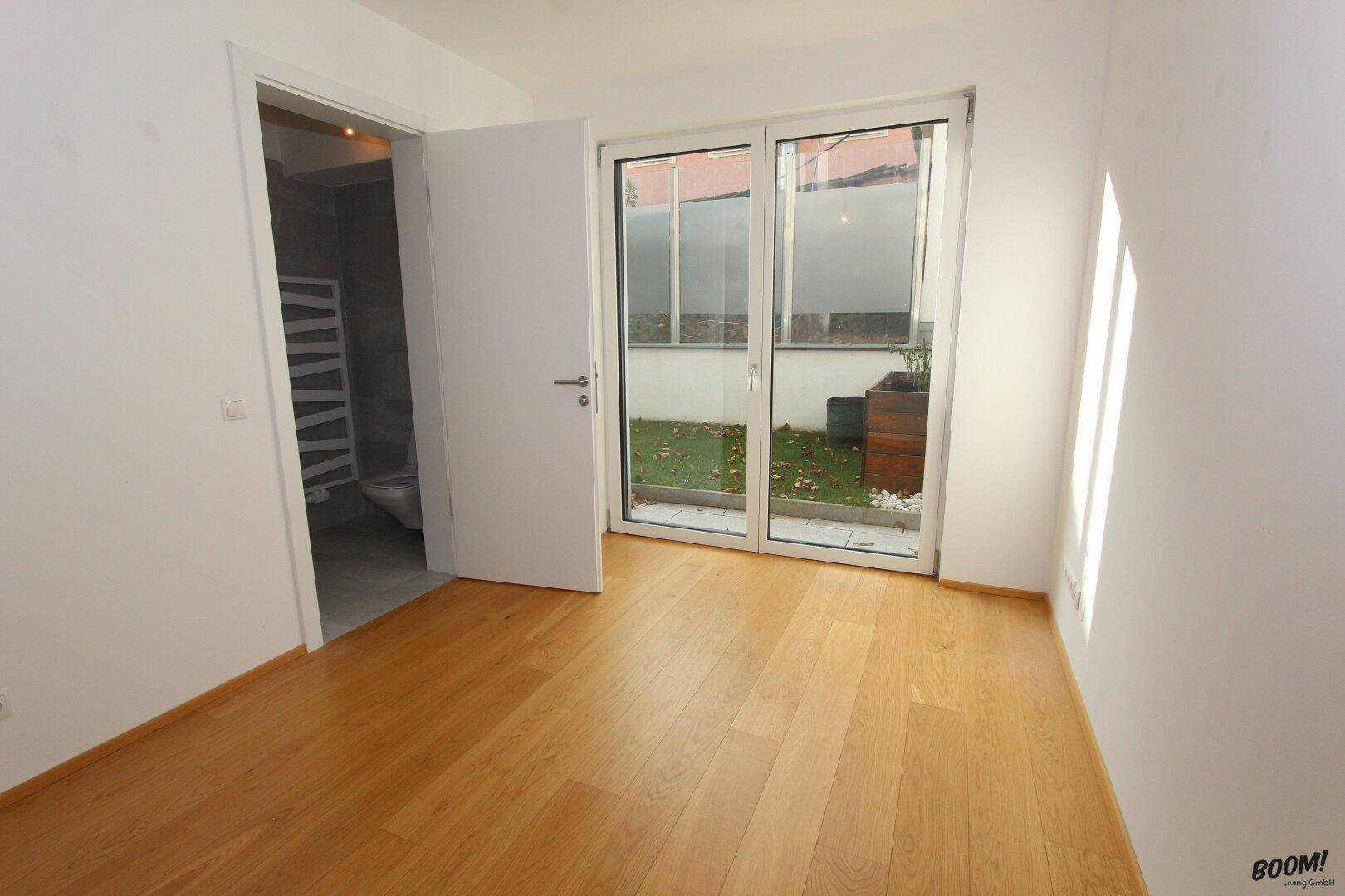 Schlafzimmer mit Parkettboden, Zugang zur Terrasse und angrenzendem modernen Badezimmer.