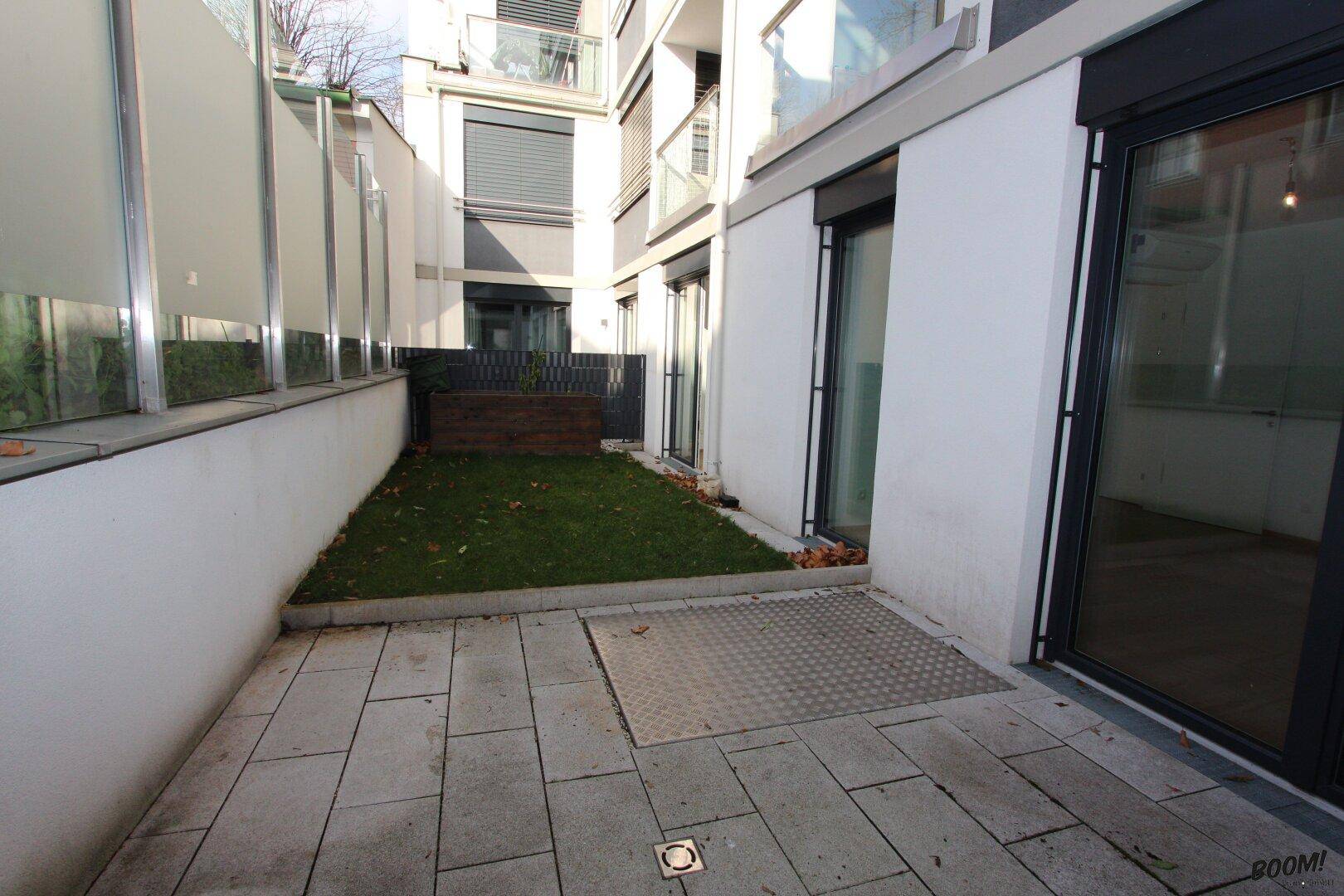Gepflasterte Terrasse mit angrenzender kleiner Rasenfläche in einem modernen Wohnkomplex.