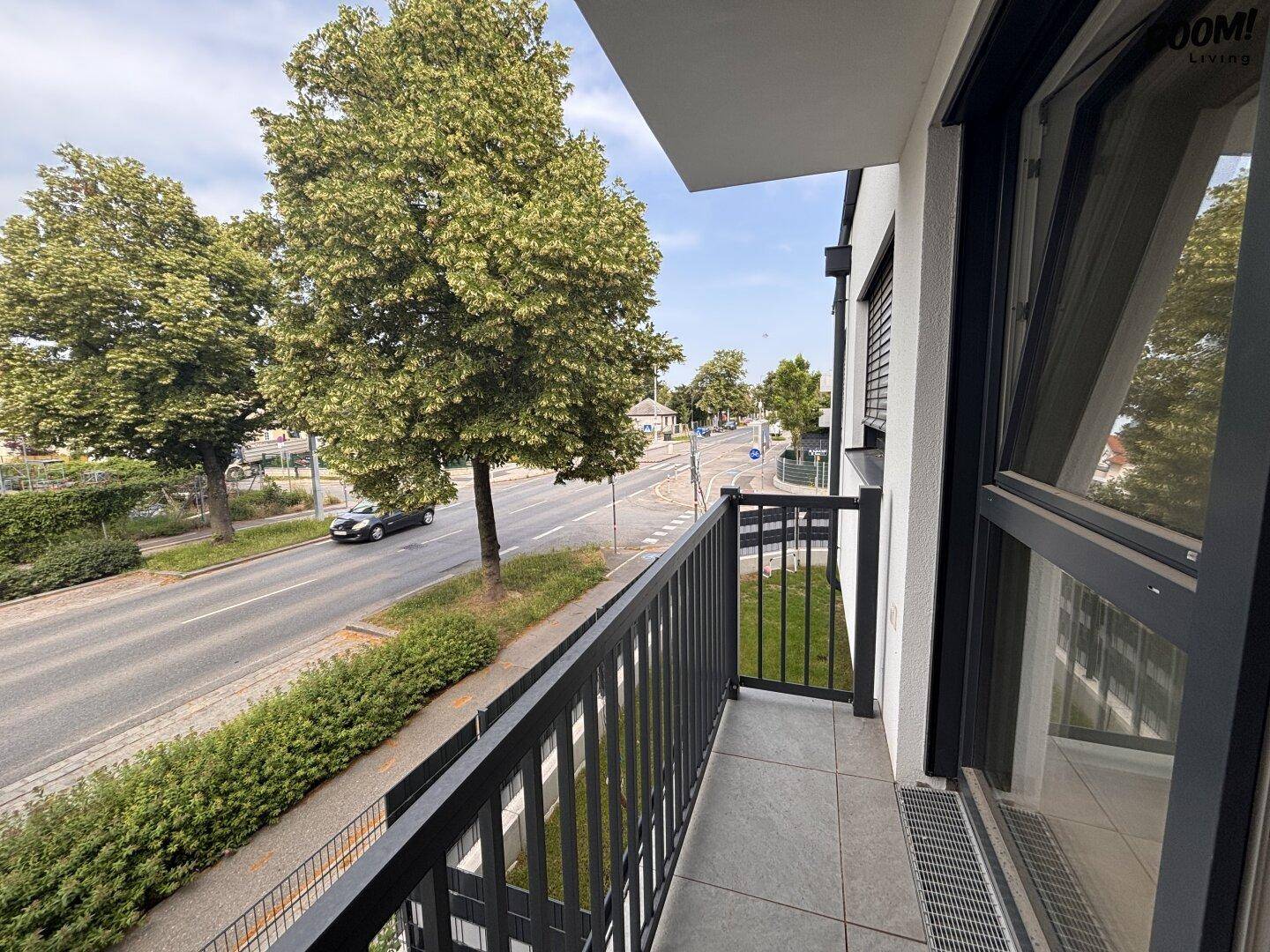 Kleiner Balkon mit modernem Geländer und Fliesenboden, bietet einen Blick auf die belebte Straße und grüne Bäume.