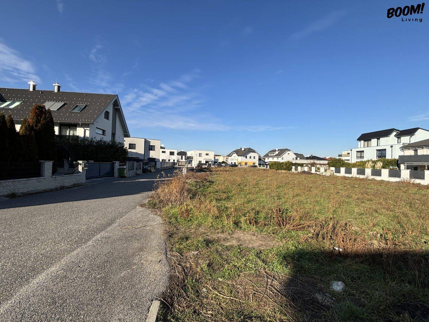 Weitläufiges unbebautes Grundstück in einer Wohngegend mit modernen Häusern und klarem Himmel, ideal für Neubau.