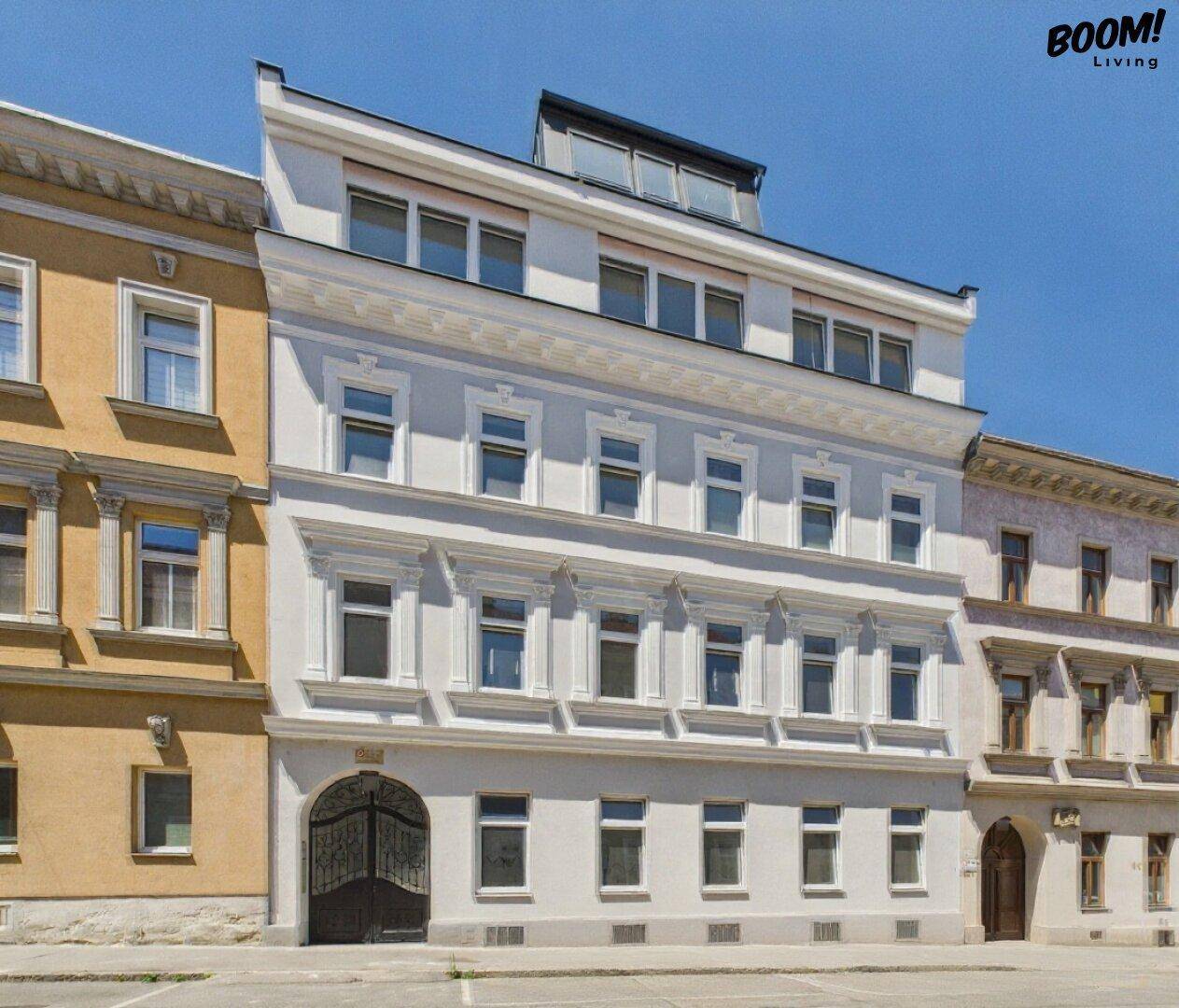Modernes Gebäude mit heller Fassade und Dachausbau unter blauem Himmel.