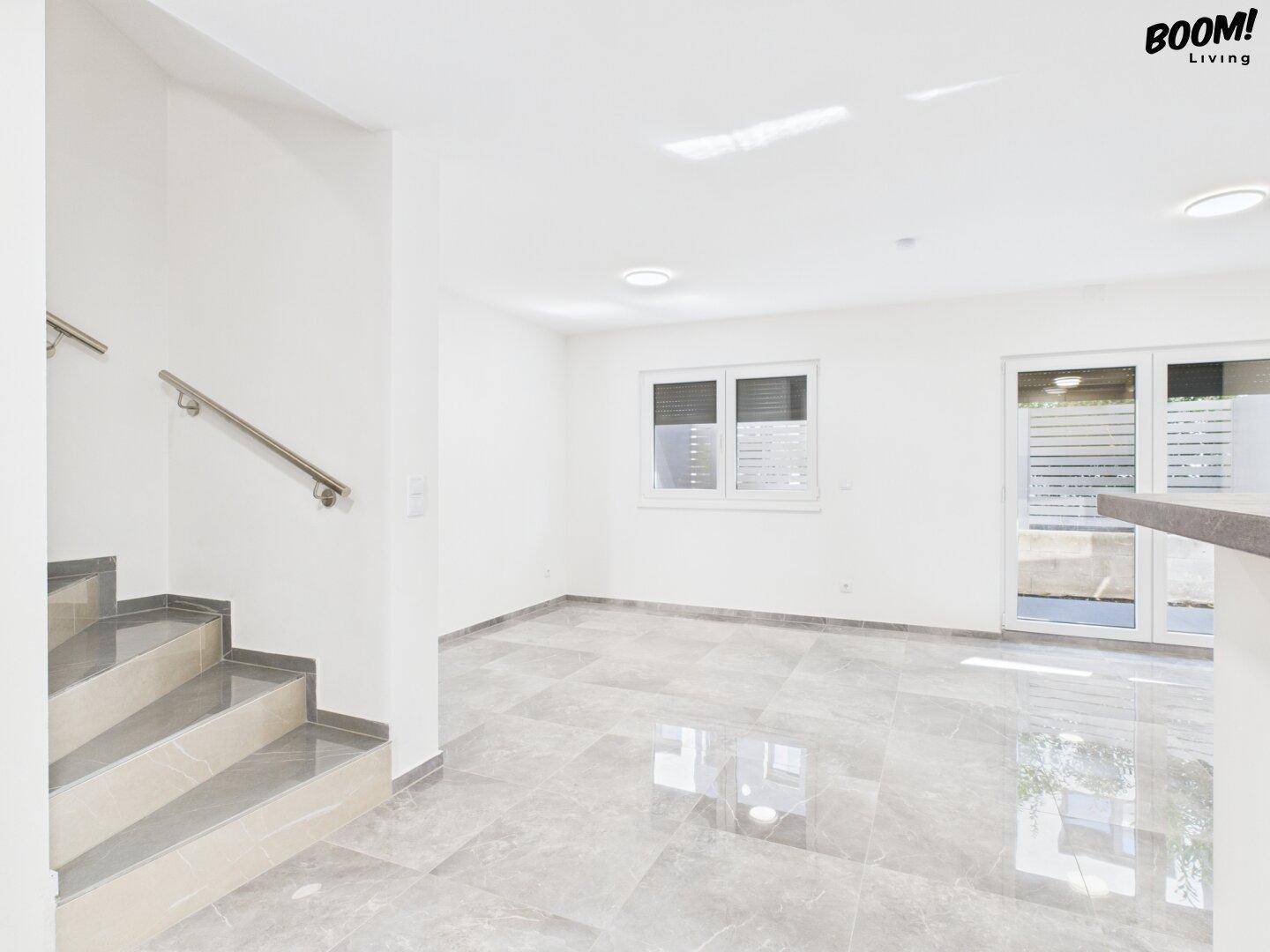 Helles, leeres Zimmer mit Fliesenboden und Zugang zu einem Außenbereich sowie einer Treppe.