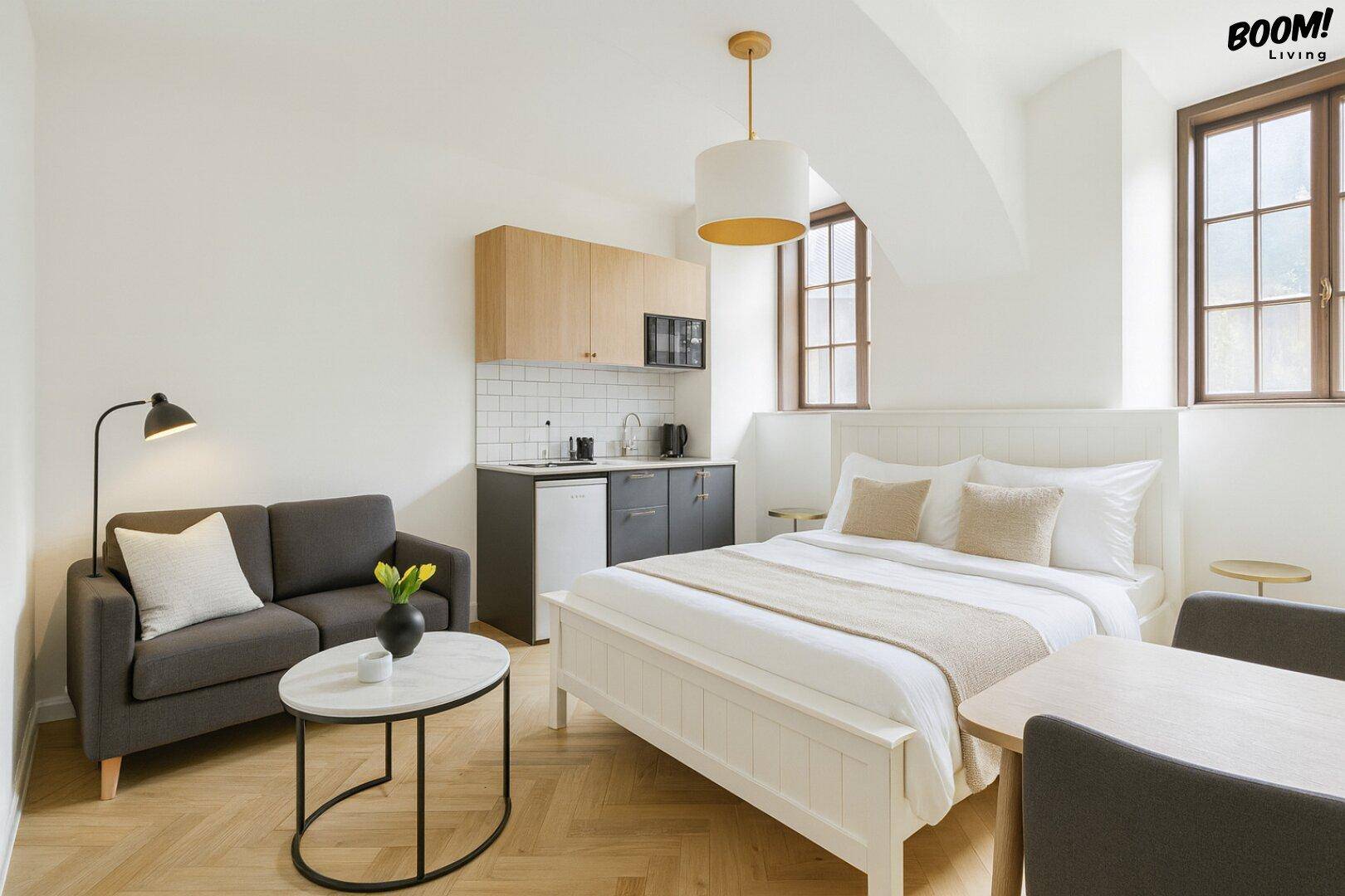 Helles Studio-Apartment mit Schlafbereich, Sofa und integrierter Küchenzeile.