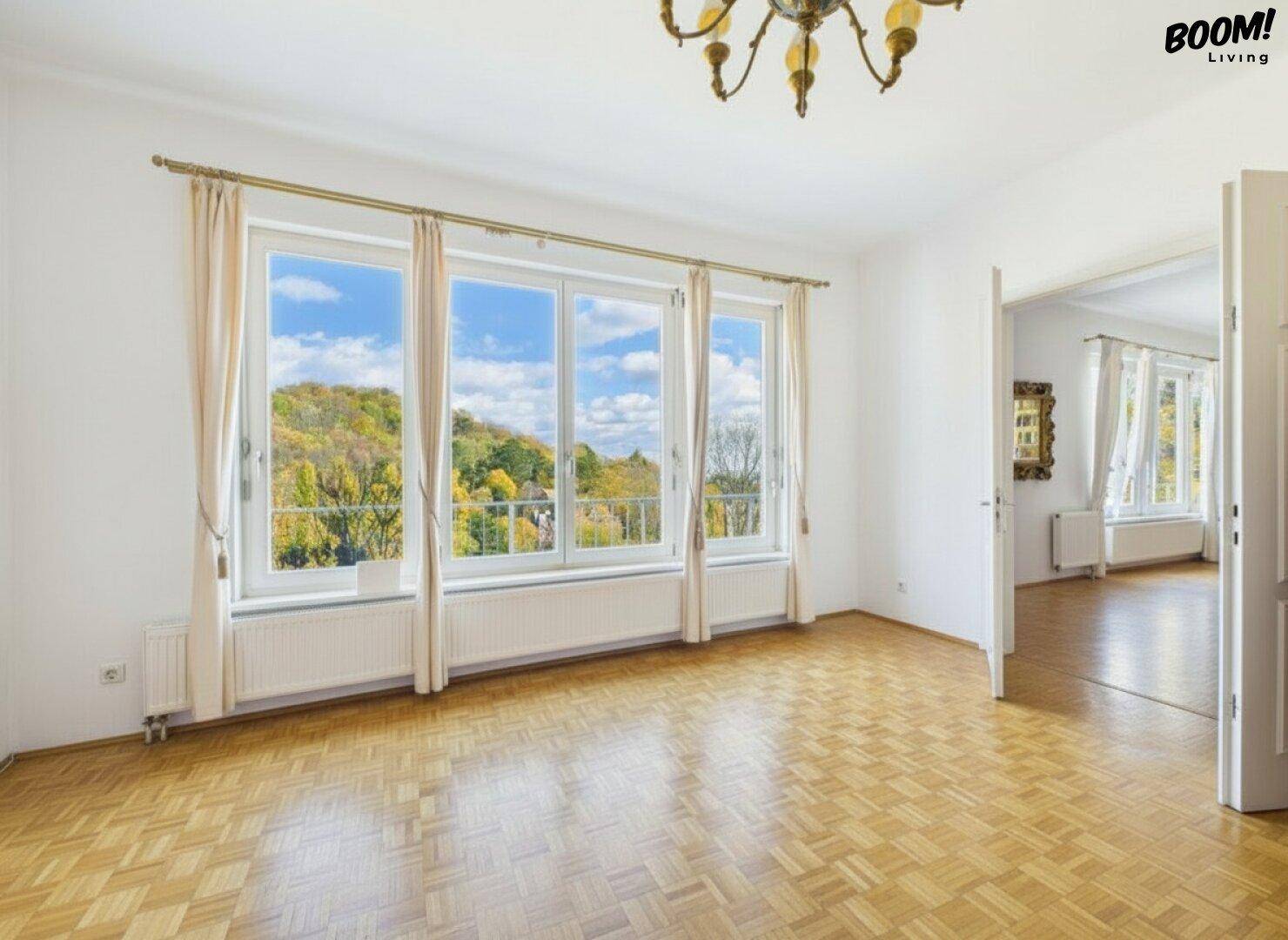 Heller Raum mit Parkettboden, großen Fenstern und einem Kronleuchter, offen zu einem weiteren Zimmer.
