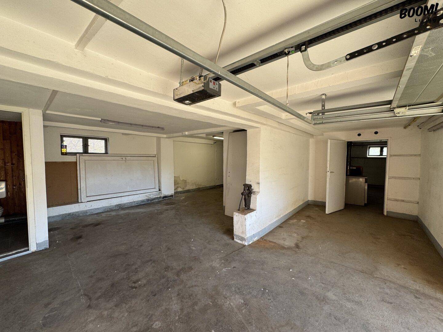 Geräumige Garage oder Kellerraum mit Betonboden, weißen Wänden und sichtbaren Garagentorführungen.