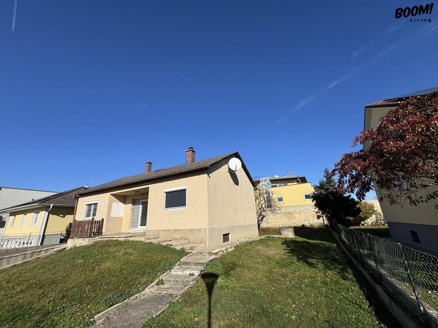 Einfamilienhaus mit beiger Fassade und Satteldach, gelegen auf einem grünen Hügel unter klarem Himmel.
