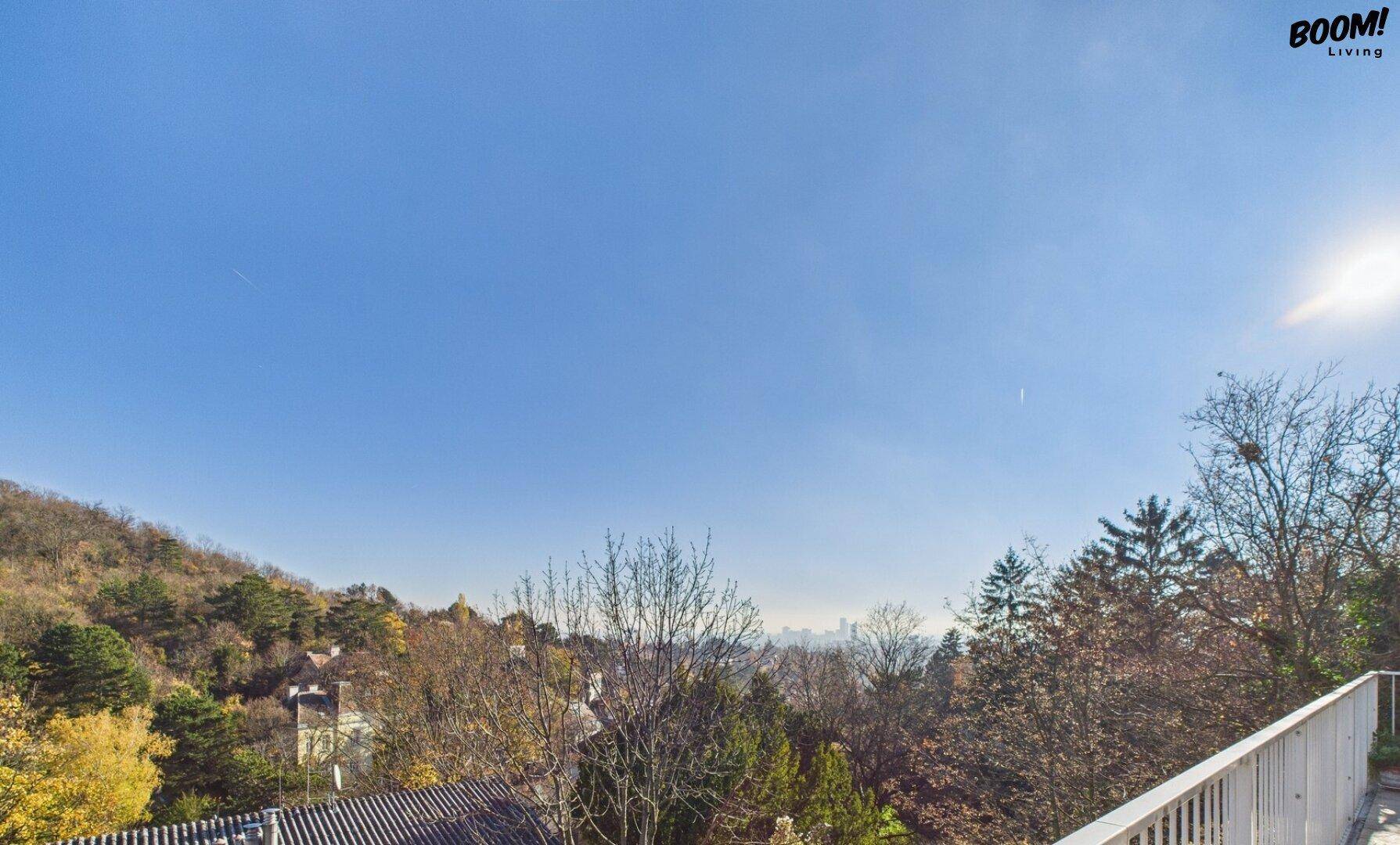 Panoramablick über bewaldete Hügel und eine ferne Stadtkulisse unter strahlendem Himmel.