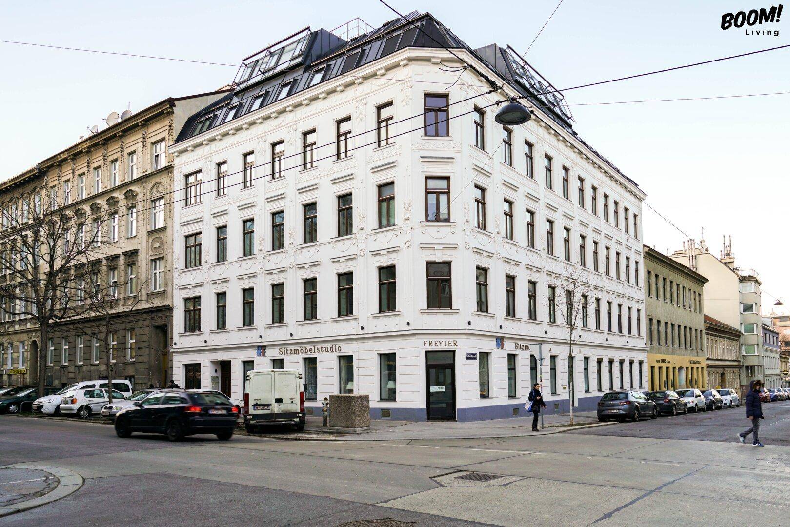 Historisches Eckgebäude mit moderner Dachaufstockung in urbaner Umgebung und vielen Fenstern.