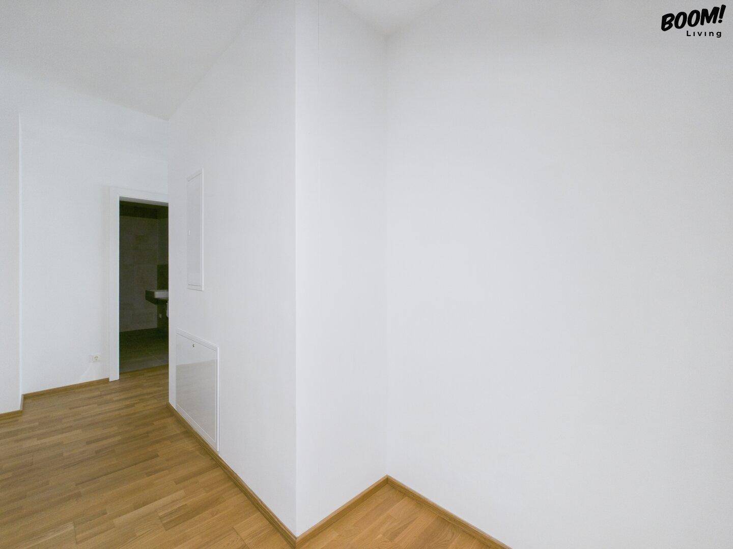 Heller Eckbereich eines Zimmers mit Parkettboden und Zugang zu einem angrenzenden Badezimmer.