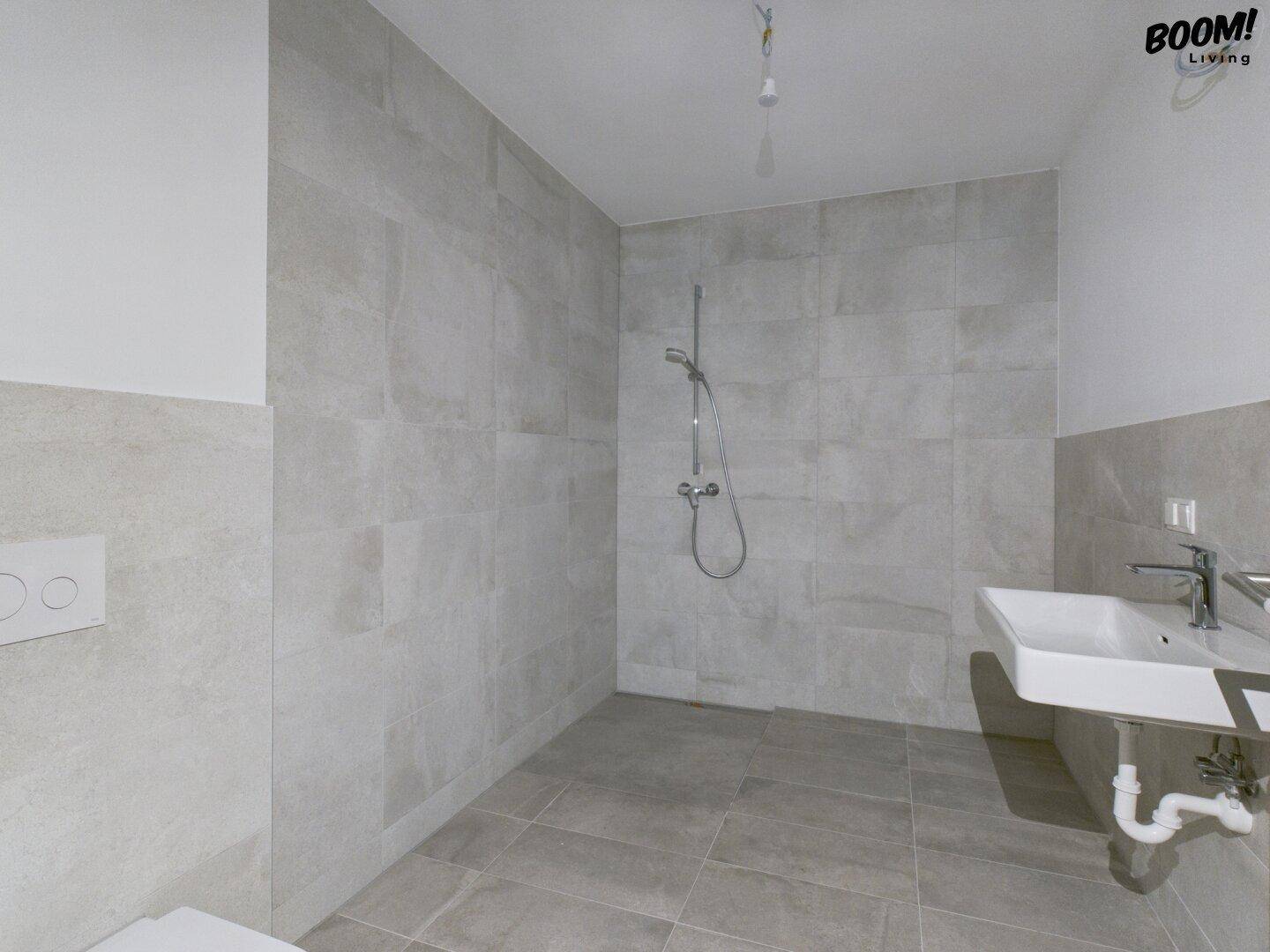 Modernes Badezimmer mit grauen Fliesen, ebenerdiger Dusche und Waschbecken.