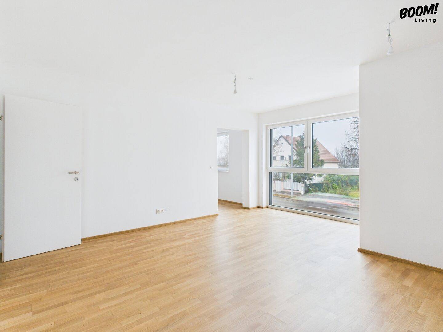 Helles Wohnzimmer mit großen Fenstern und Blick auf die Straße, ausgestattet mit Parkettboden.