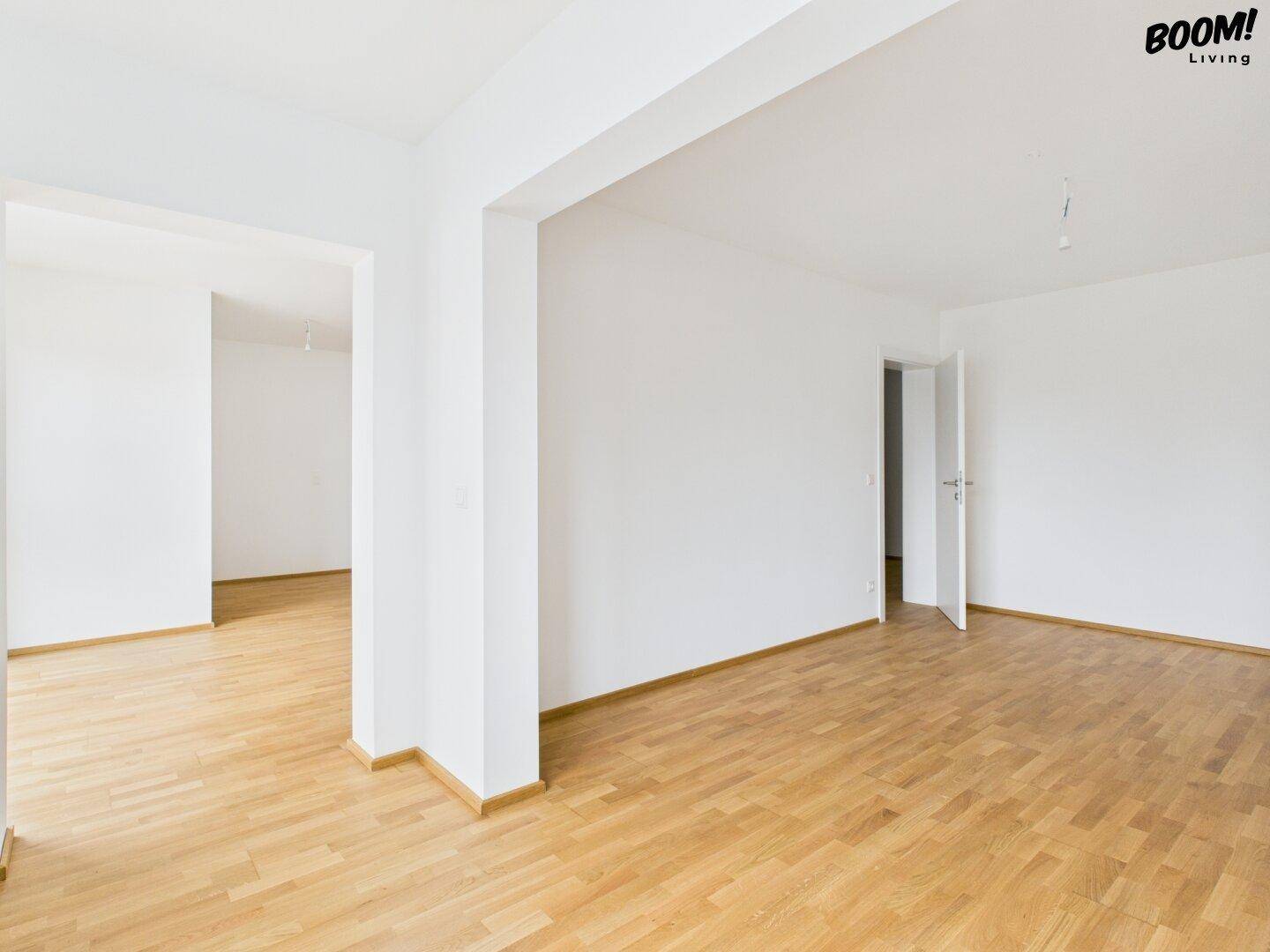 Geräumiger Wohnbereich mit Parkettboden und offenem Übergang zu einem weiteren Zimmer.