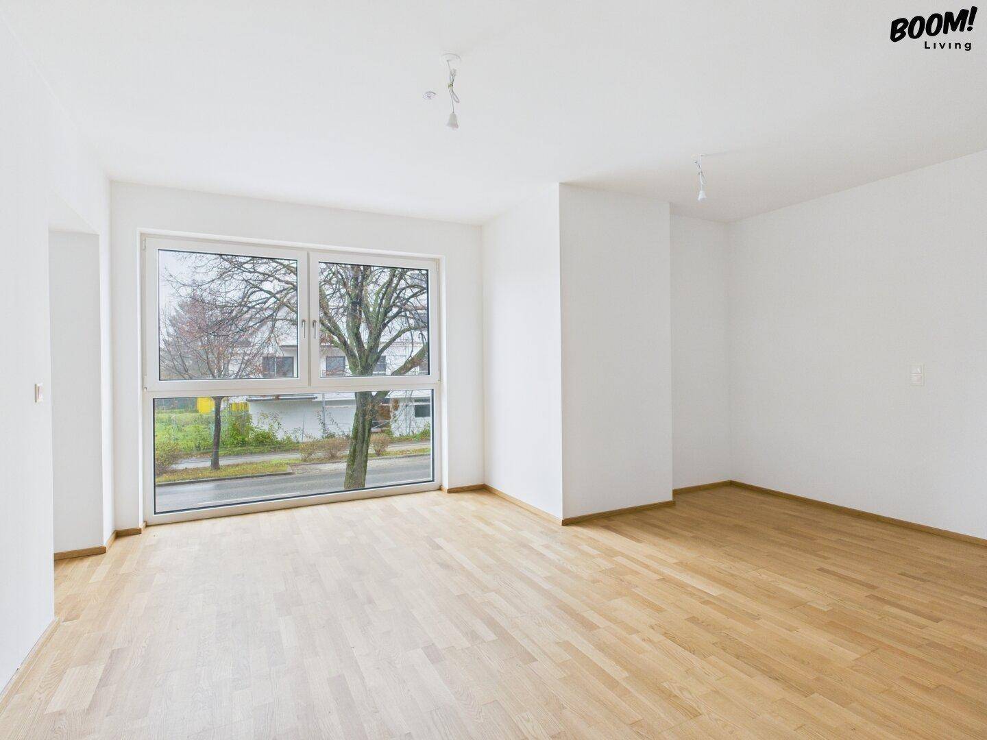 Lichtdurchflutetes Wohnzimmer mit großen Fenstern und Parkettboden.