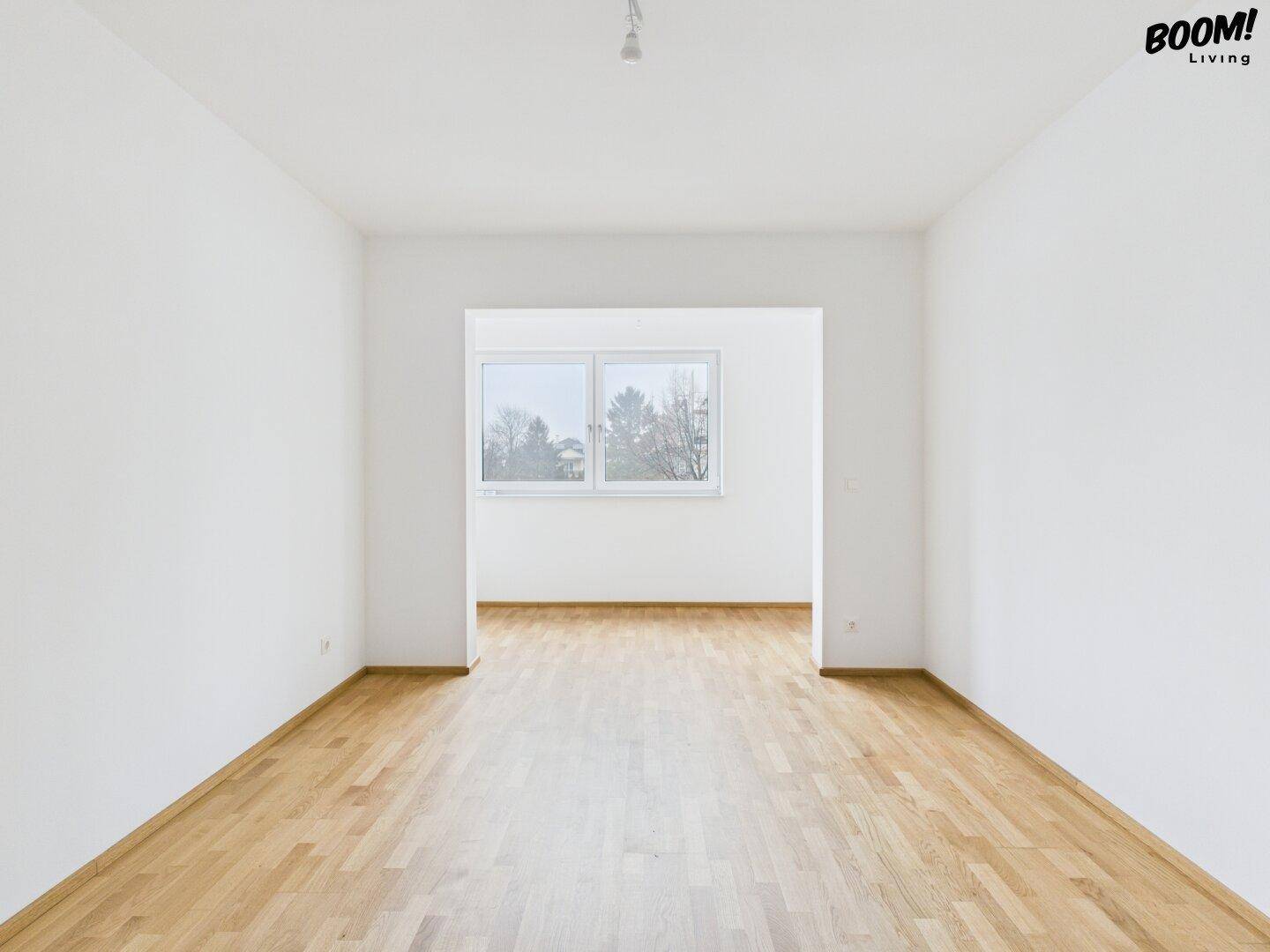 Geräumiger, heller Raum mit Holzboden und offenem Durchgang zu einem weiteren Zimmer.