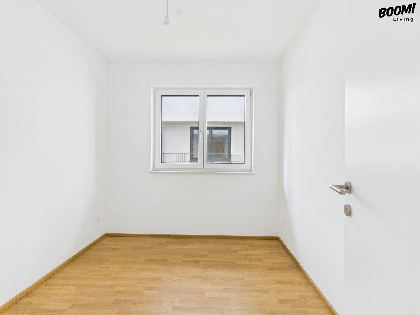 Helles, leeres Zimmer mit Holzboden und Fenster, ideal als Schlaf- oder Kinderzimmer.