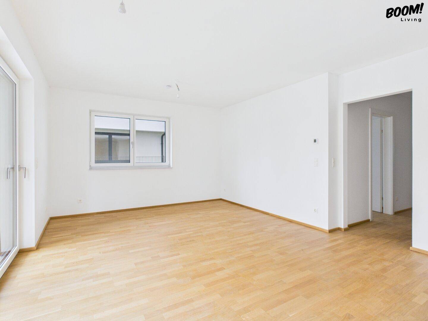 Großer, heller Wohnbereich mit Holzboden und Fenster, bereit zur individuellen Gestaltung.