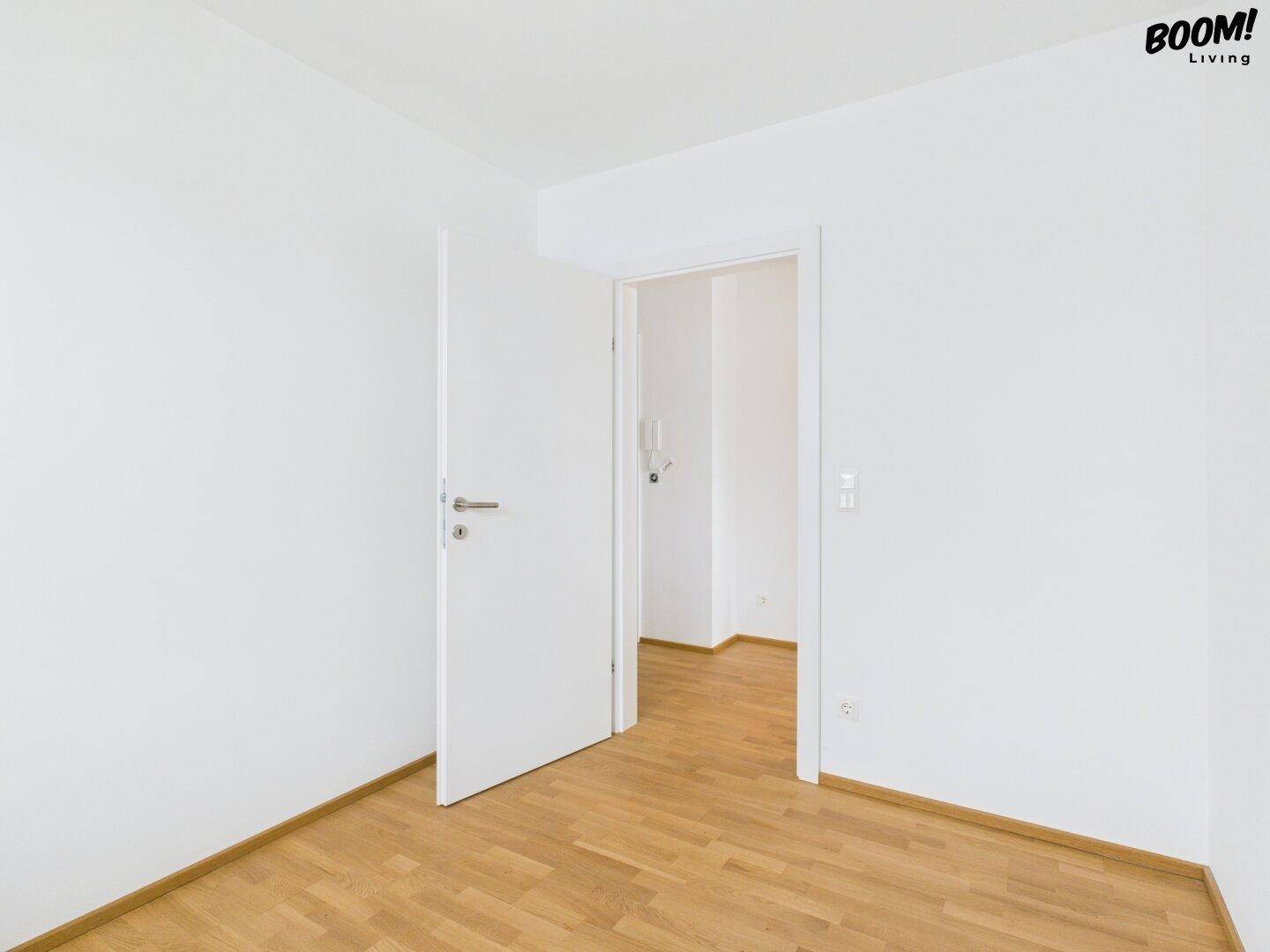 Leeres, helles Zimmer mit Holzboden und weiß gestrichenen Wänden.