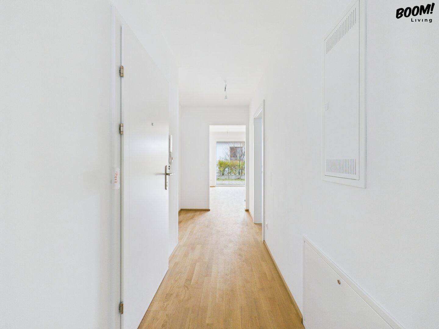 Langer, heller Flur mit Holzboden und Eingangstür, der zu den Wohnbereichen führt.