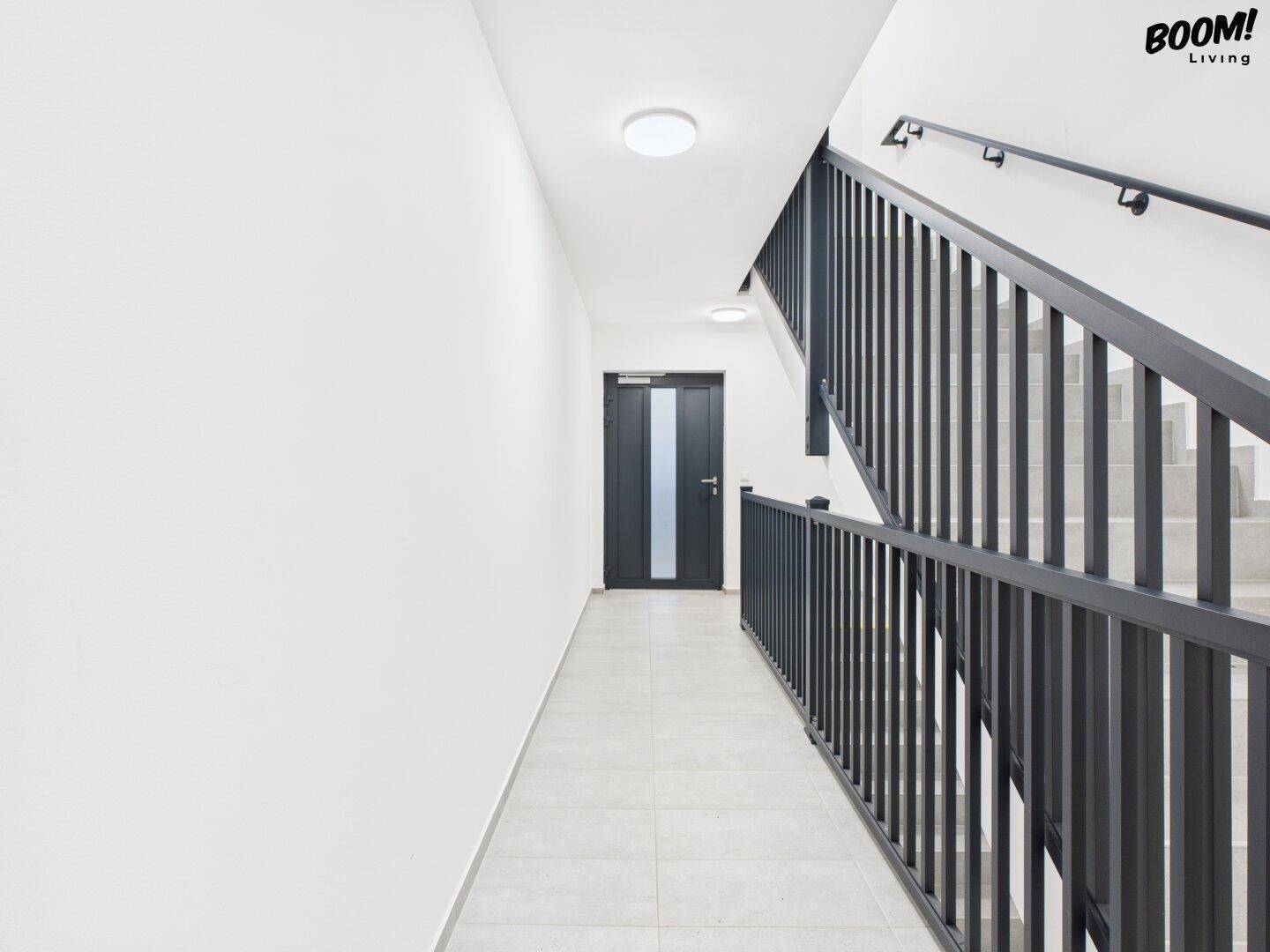 Modernes Treppenhaus mit hellem Fliesenboden und schwarzem Geländer in einem Neubau.