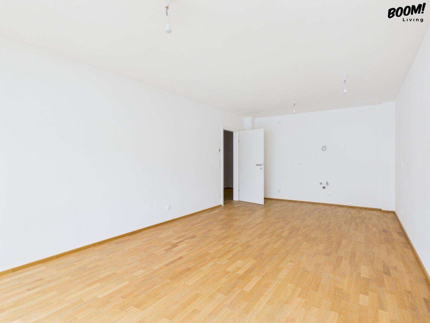 Großes, leeres Zimmer mit Holzboden und weiß gestrichenen Wänden.