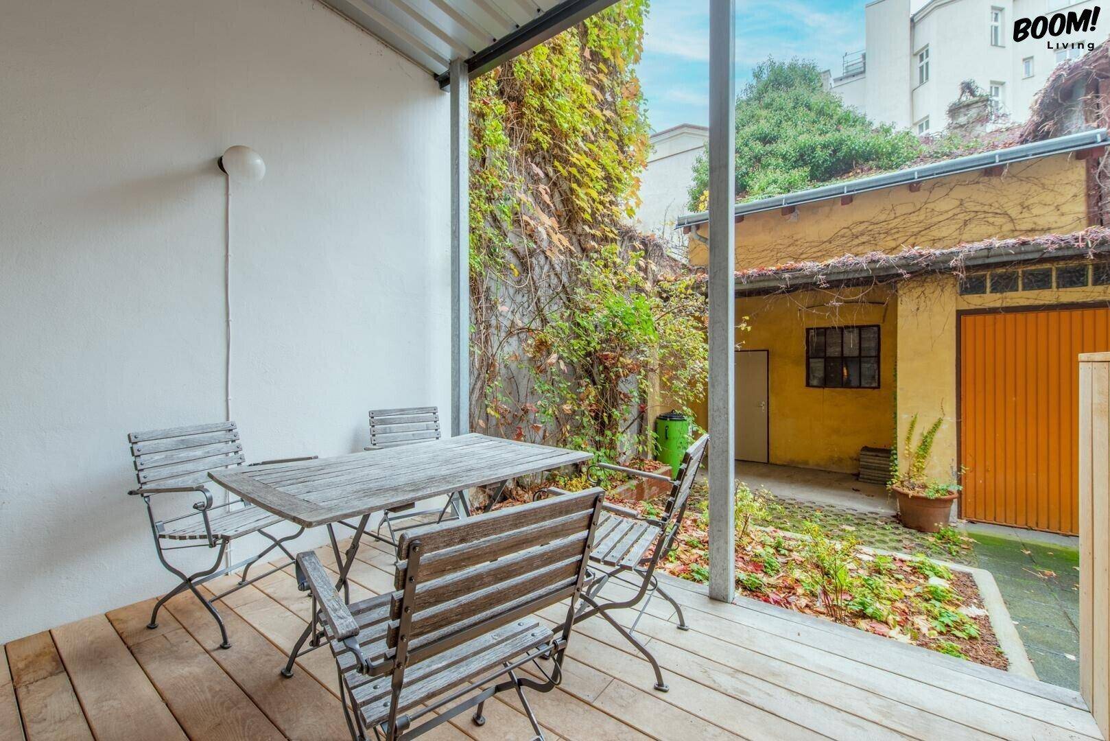 Gemütliche Terrasse mit Holzdeck und Gartenmöbeln, umgeben von üppigem Grün und alten Mauern.
