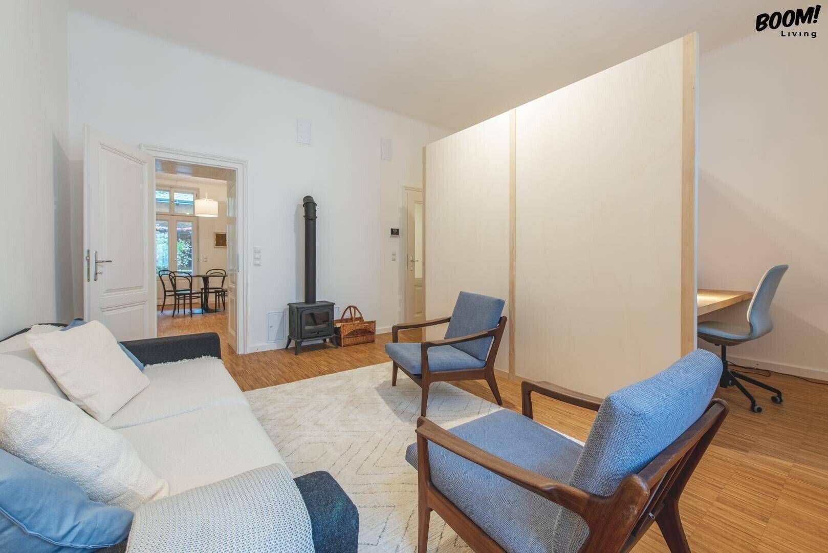 Gemütlicher Wohnbereich mit Sofa, Sesseln und einem Raumteiler, der einen Arbeitsbereich abtrennt.