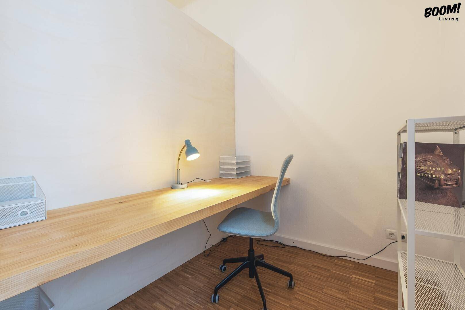 Funktionaler Arbeitsbereich mit einem langen Holzschreibtisch, Bürostuhl und Regal für Stauraum.