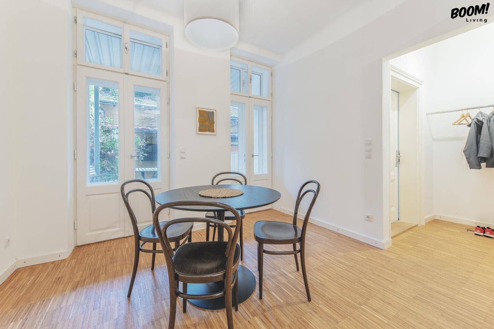 Heller Essbereich mit einem runden Tisch und Stühlen, umgeben von großen Fenstertüren zum Außenbereich.