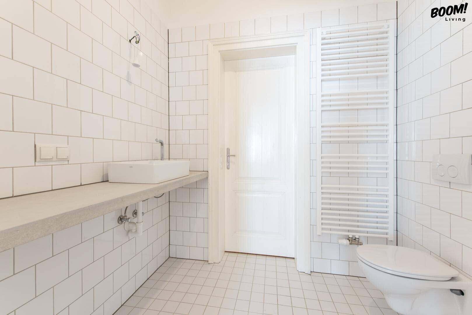 Helles Badezimmer mit weißen Fliesen, modernem Waschbecken und beheiztem Handtuchhalter.