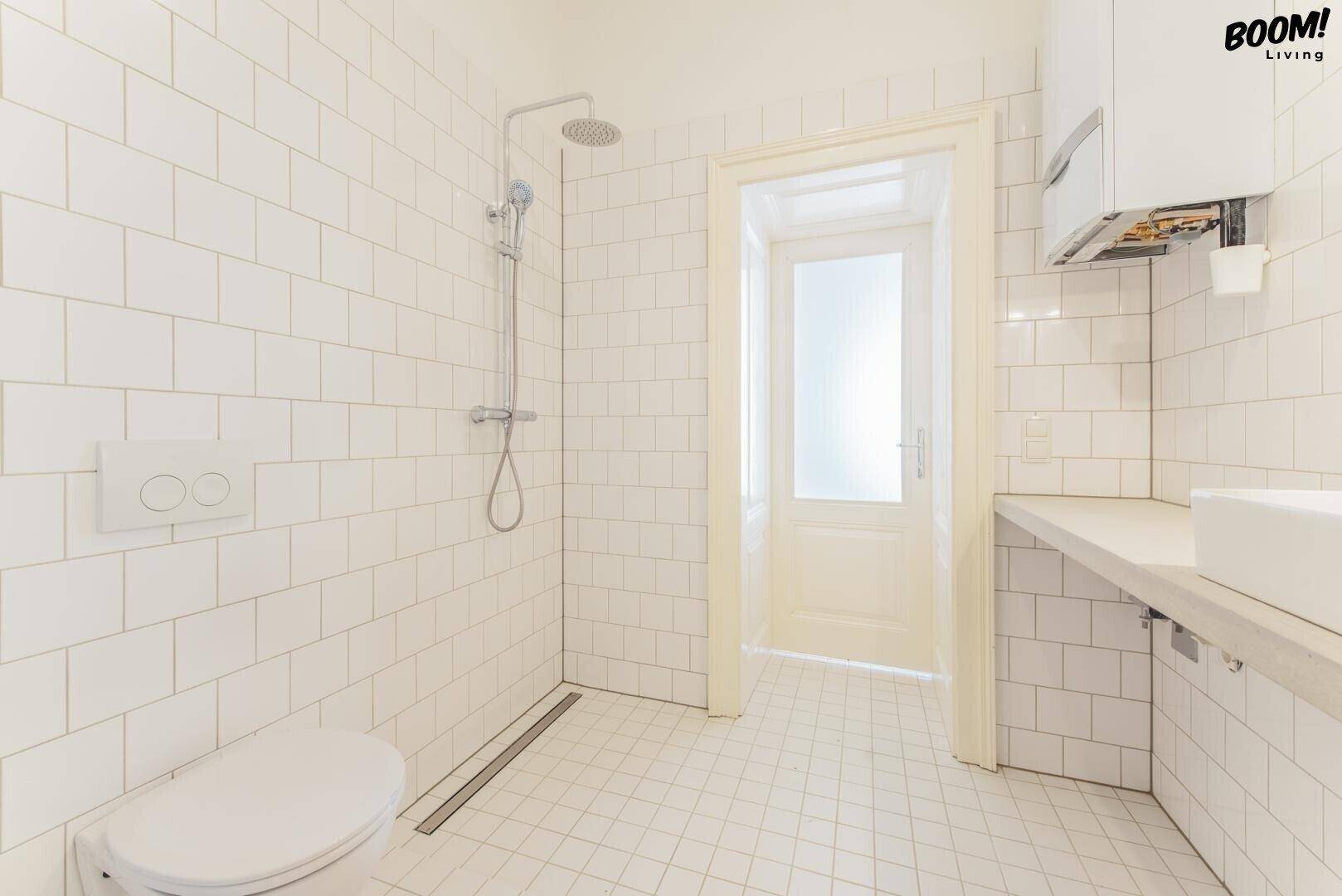 Modernes Badezimmer mit weißen Fliesen, ebenerdiger Dusche und wandhängendem WC.