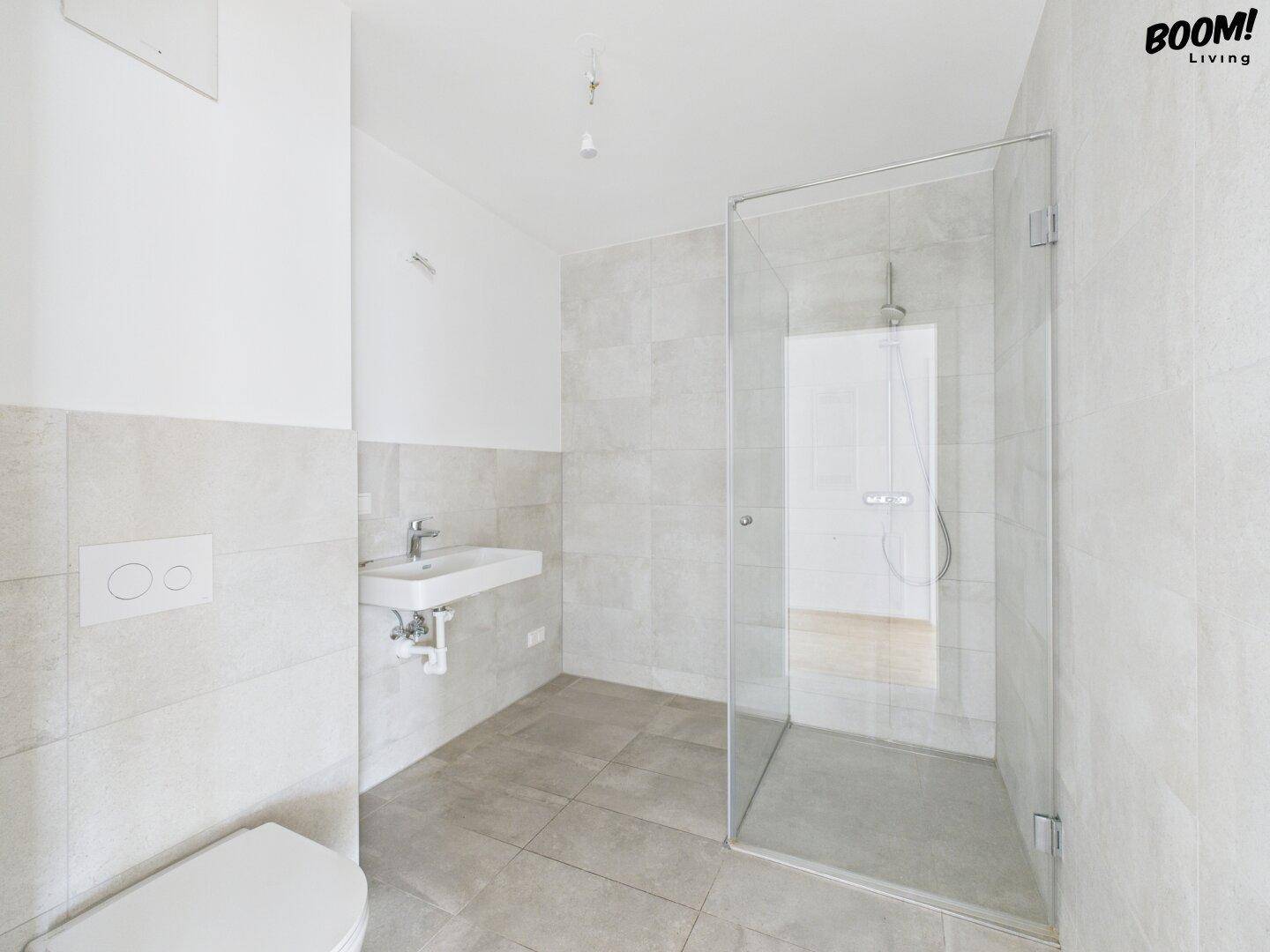 Modernes Badezimmer mit begehbarer Dusche, Wand-WC und hellen Fliesen an Wänden und Boden.