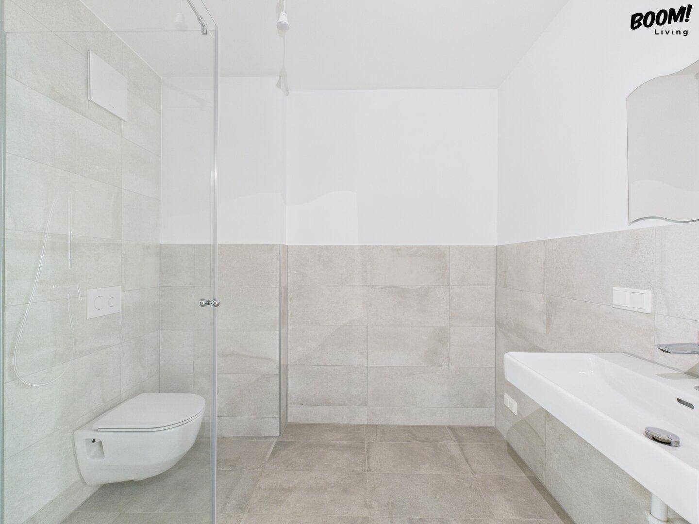 Modernes Badezimmer mit hellgrauen Fliesen, bodengleicher Dusche und wandhängendem WC.