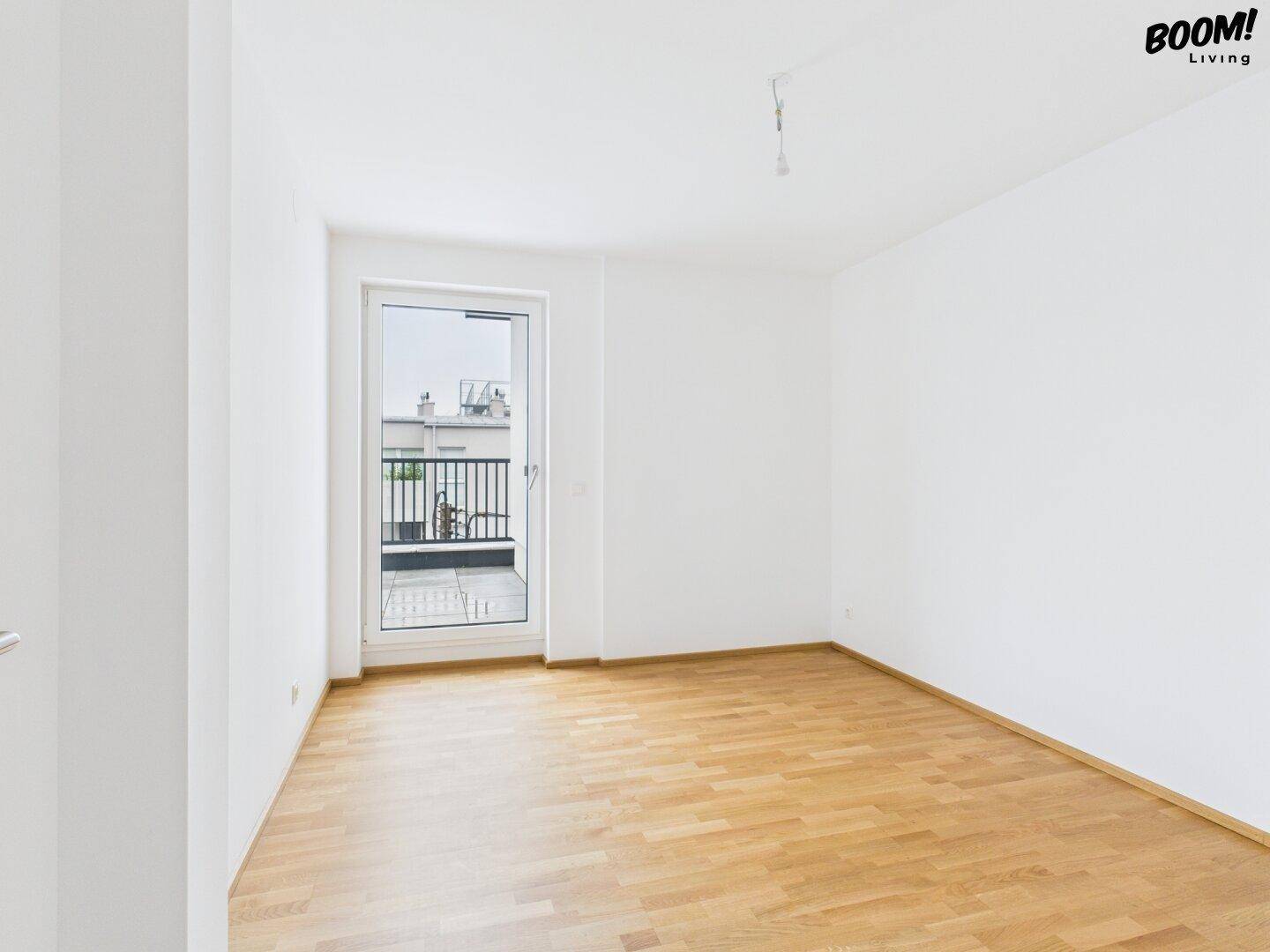 Helles, leeres Zimmer mit Holzboden und Balkonzugang, bereit zur individuellen Gestaltung.