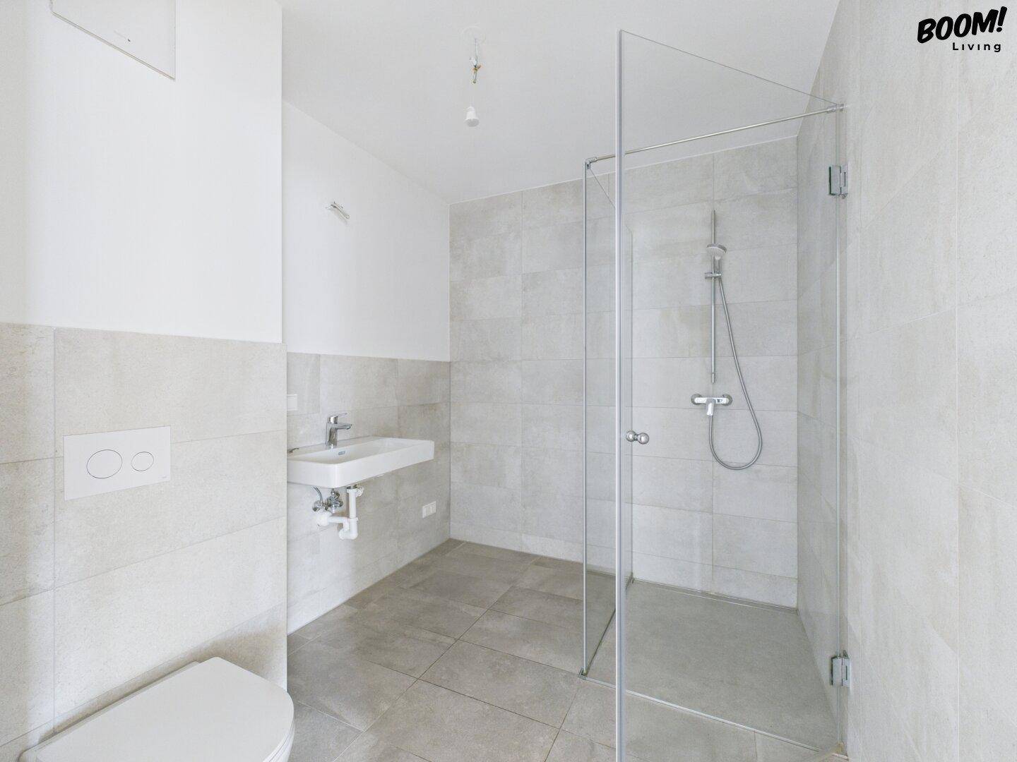 Unmöbliertes Badezimmer mit begehbarer Dusche, Wand-WC und modernen Fliesen.