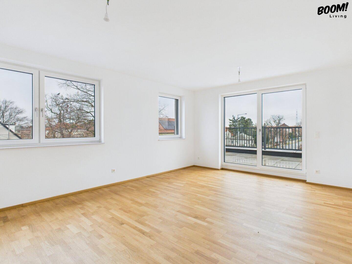Helles, unmöbliertes Zimmer mit Holzboden und Zugang zu einem großen Balkon.