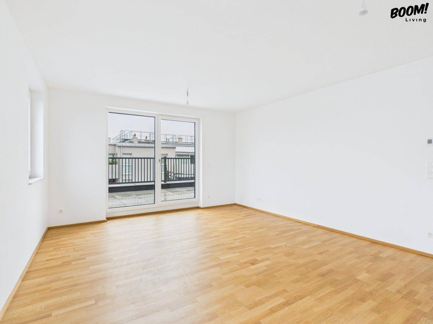 Leeres Zimmer mit Holzboden und Zugang zu einem Balkon, ideal für Schlaf- oder Arbeitsbereich.