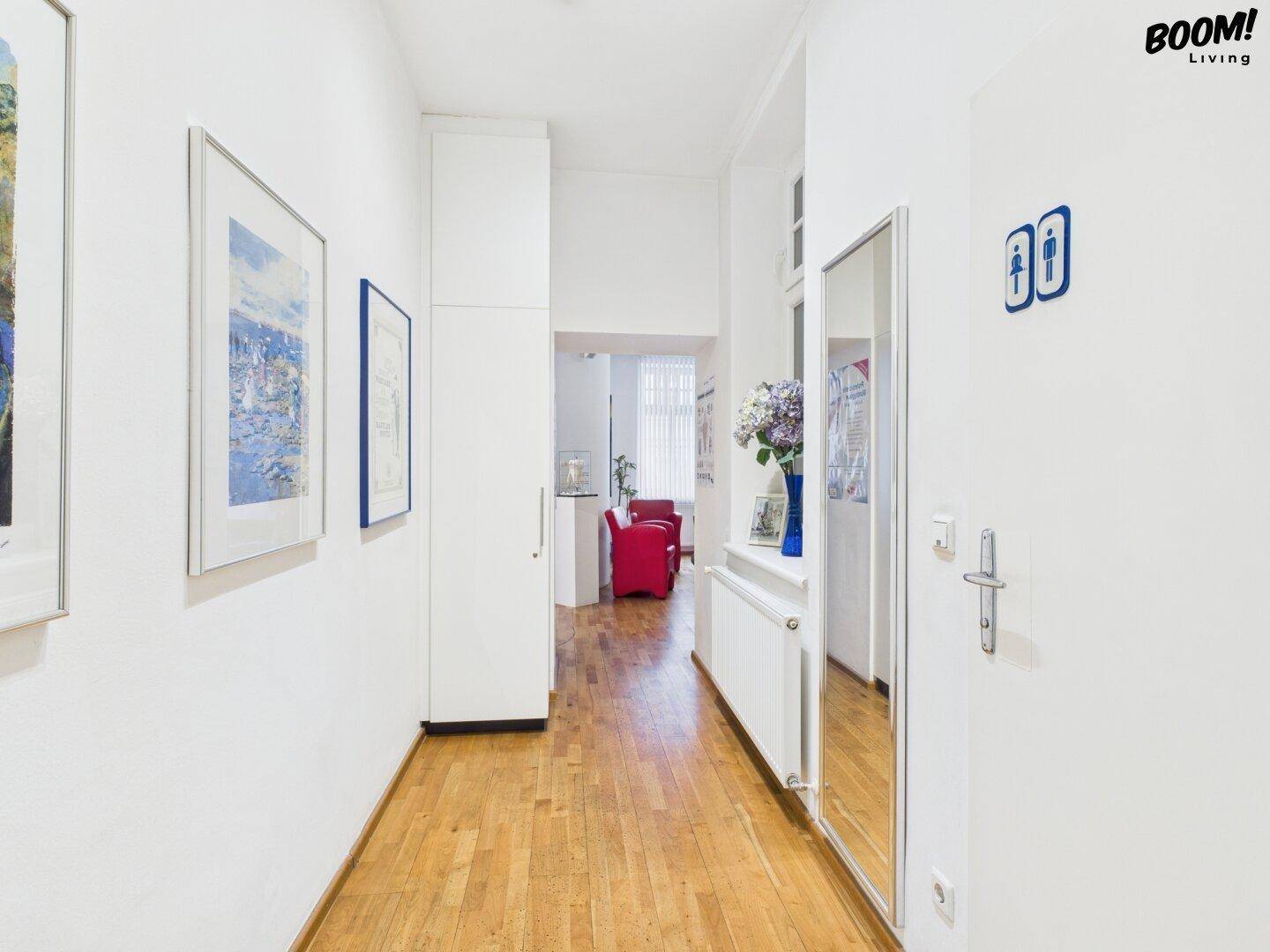 Langer Flur mit Holzfußboden, weißem Einbauschrank und einem großen Spiegel.